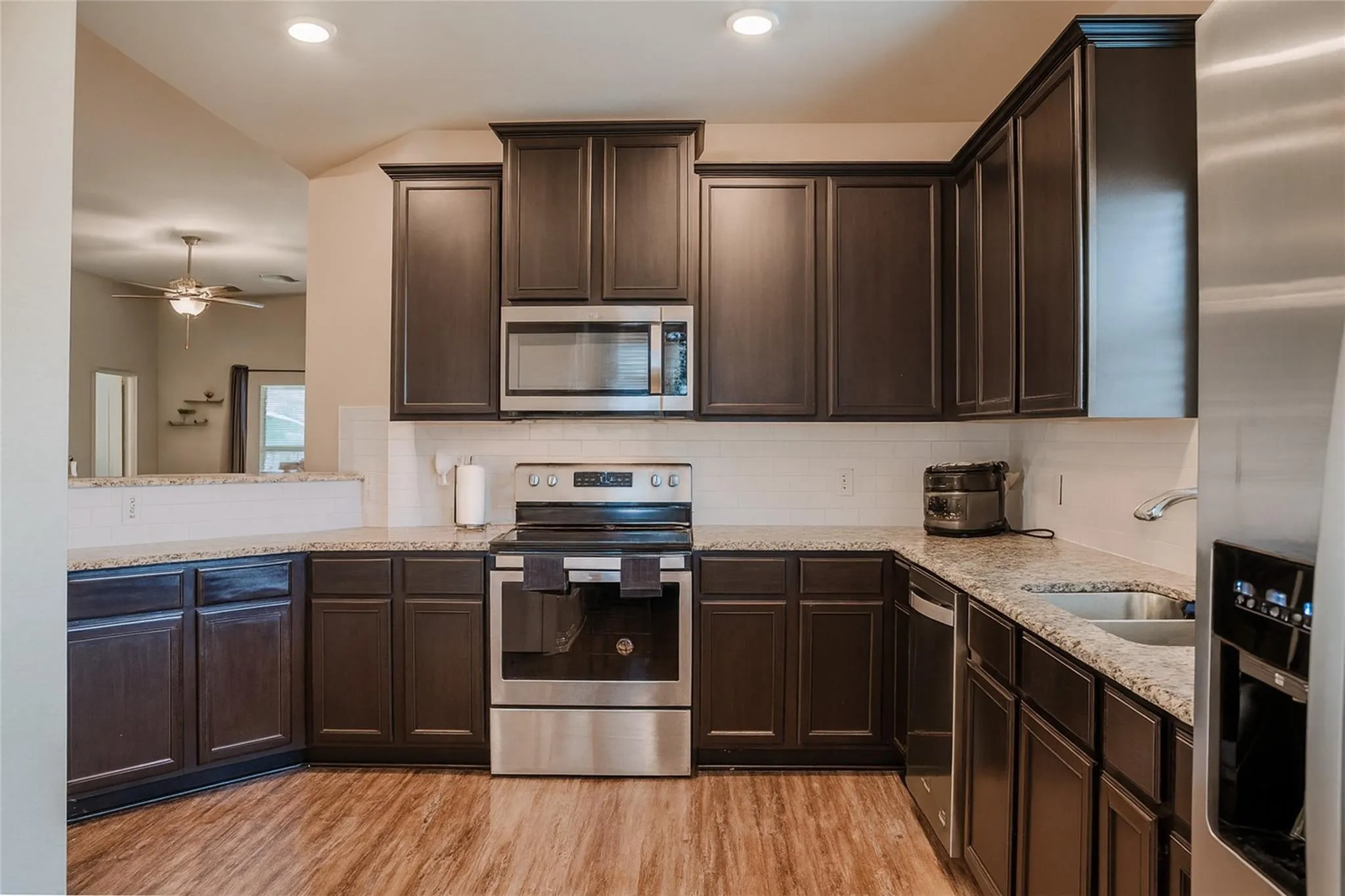 Kitchen featuring dark wood-finish cabinetry, light-toned countertops, stainless steel appliances, and wood-finish flooring