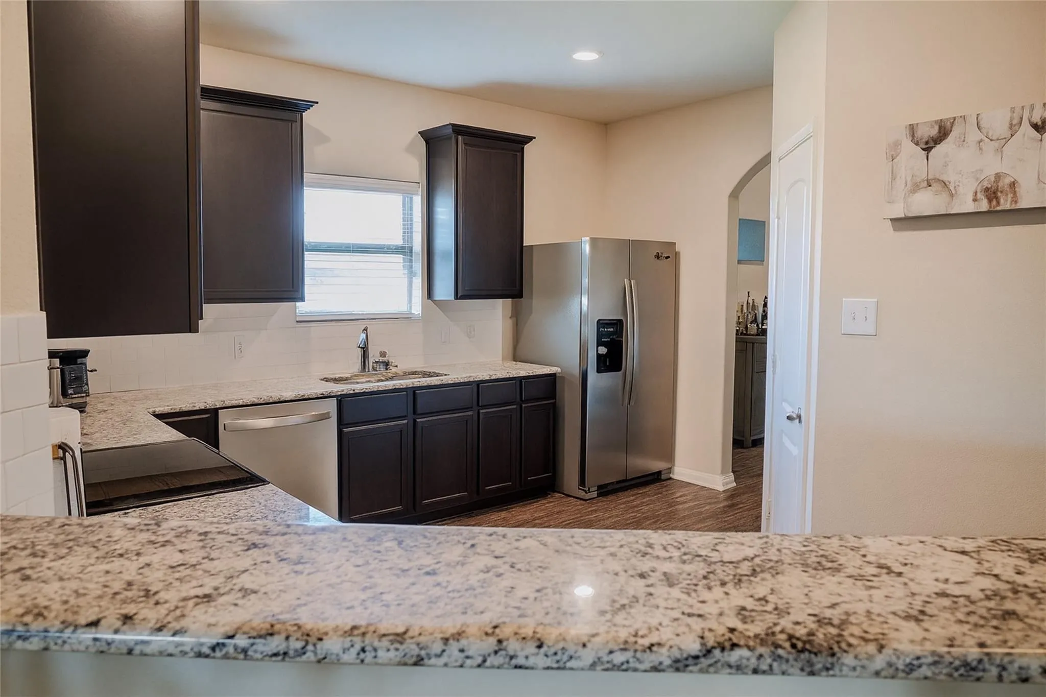 Kitchen featuring dark wood cabinetry, light-toned granite countertops, stainless steel appliances, and wood-finish flooring