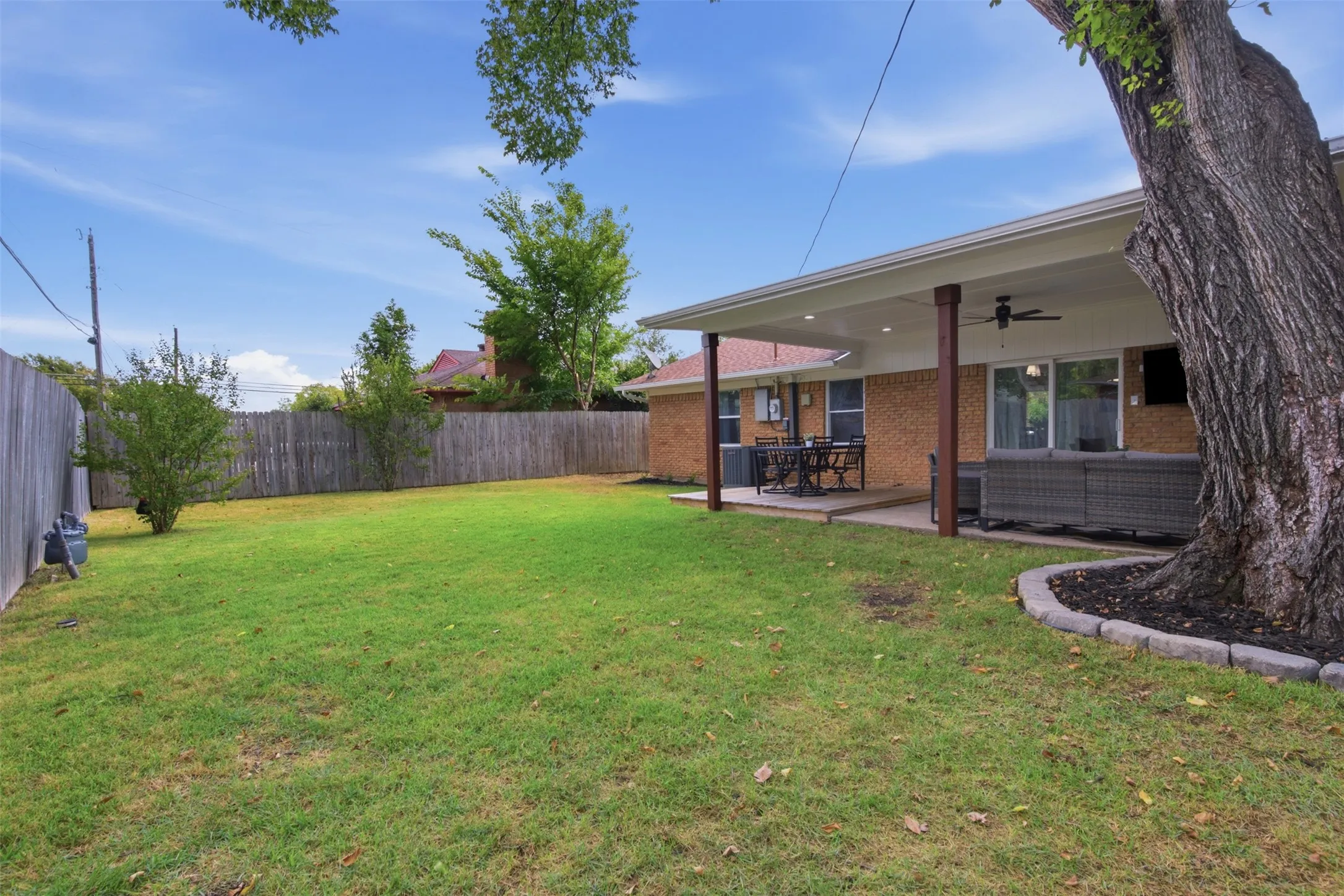 Expansive backyard featuring a covered patio, ceiling fan, brick exterior, and wood privacy fencing