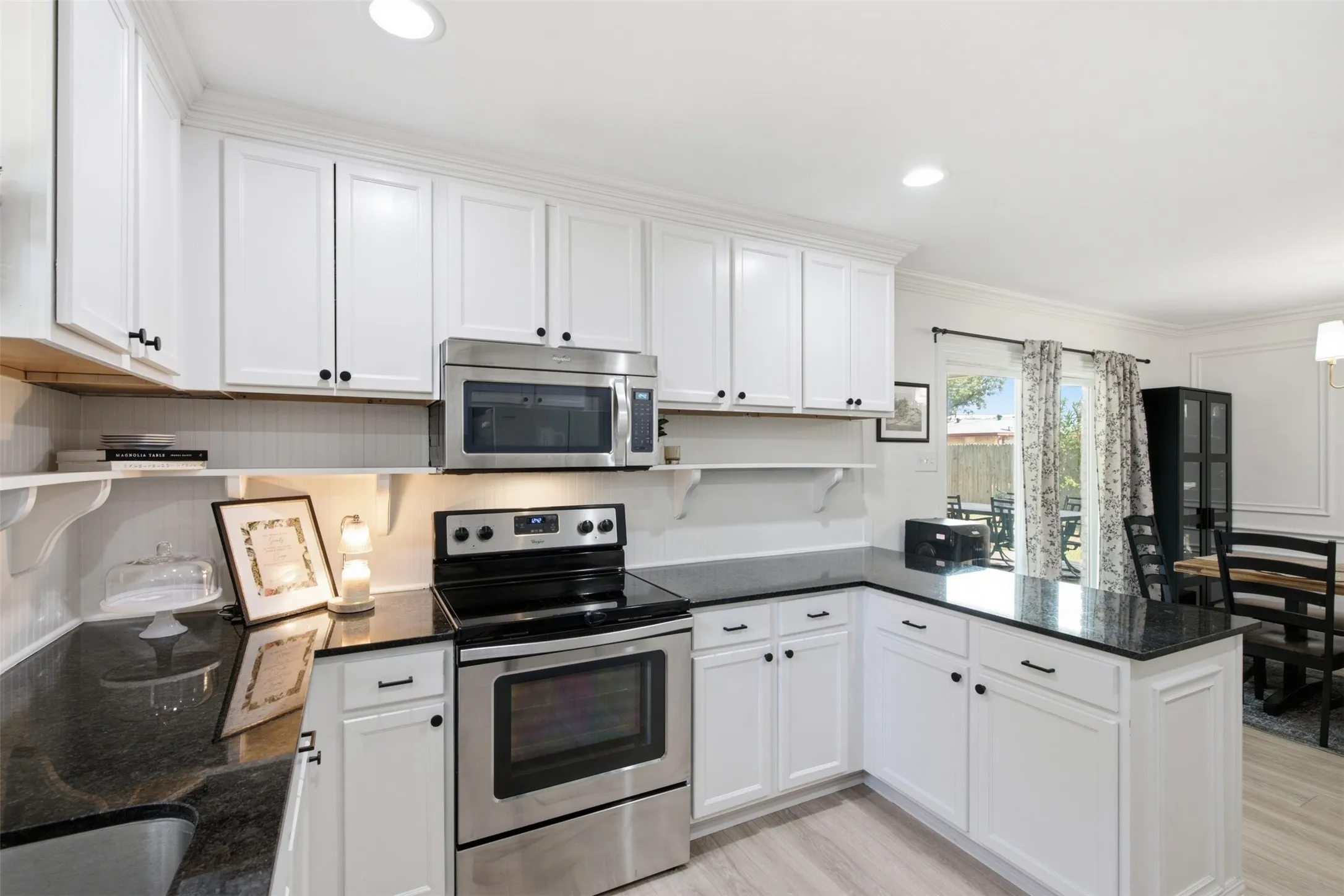 White cabinetry with black hardware, dark countertops, stainless steel appliances, and light wood-finish flooring