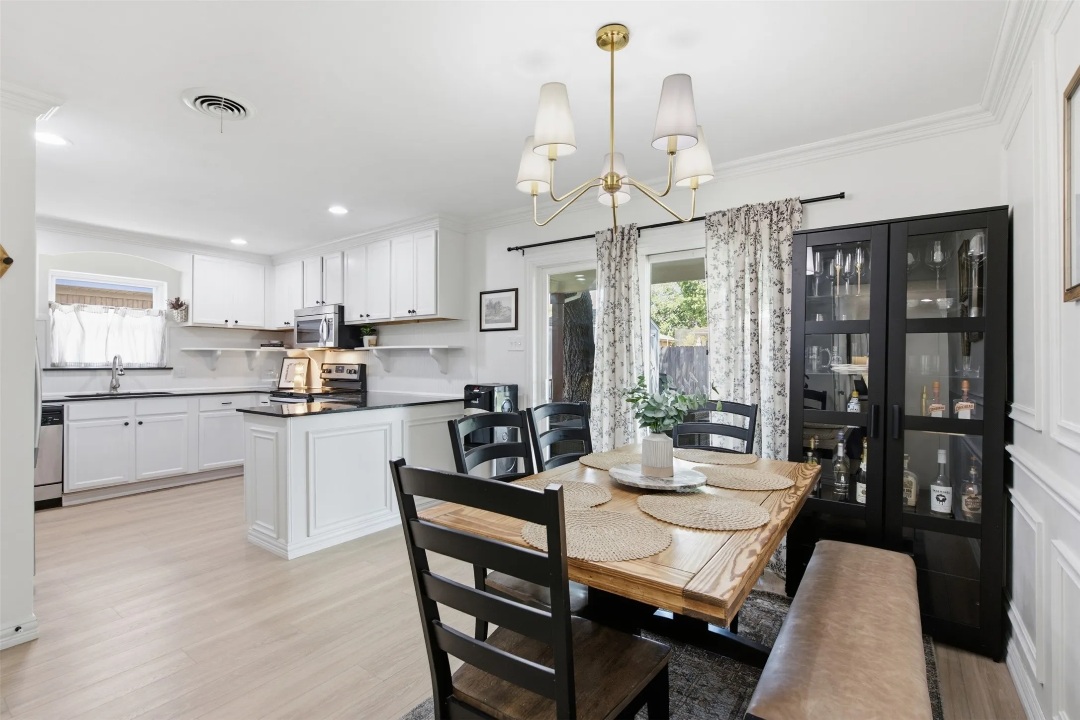White shaker cabinetry with dark countertops, light wood-finish flooring, and a brass-tone chandelier