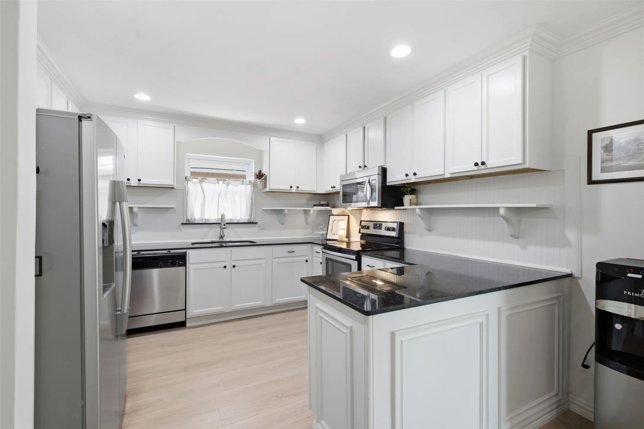 White shaker-style cabinetry, dark countertops, wood-finish flooring, and stainless steel appliances
