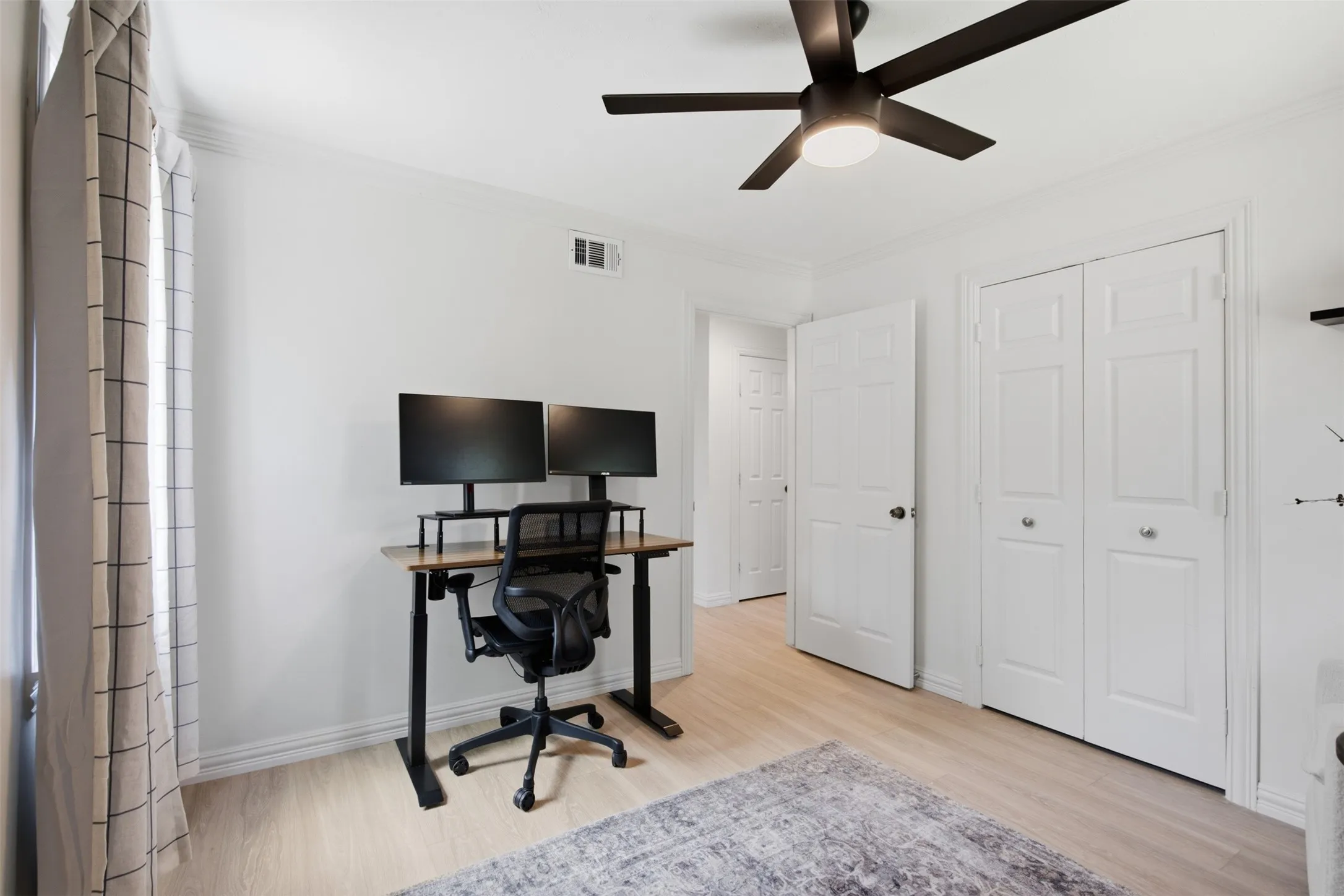 Light wood-finish flooring, white walls, bi-fold closet doors, and a ceiling fan with integrated lighting