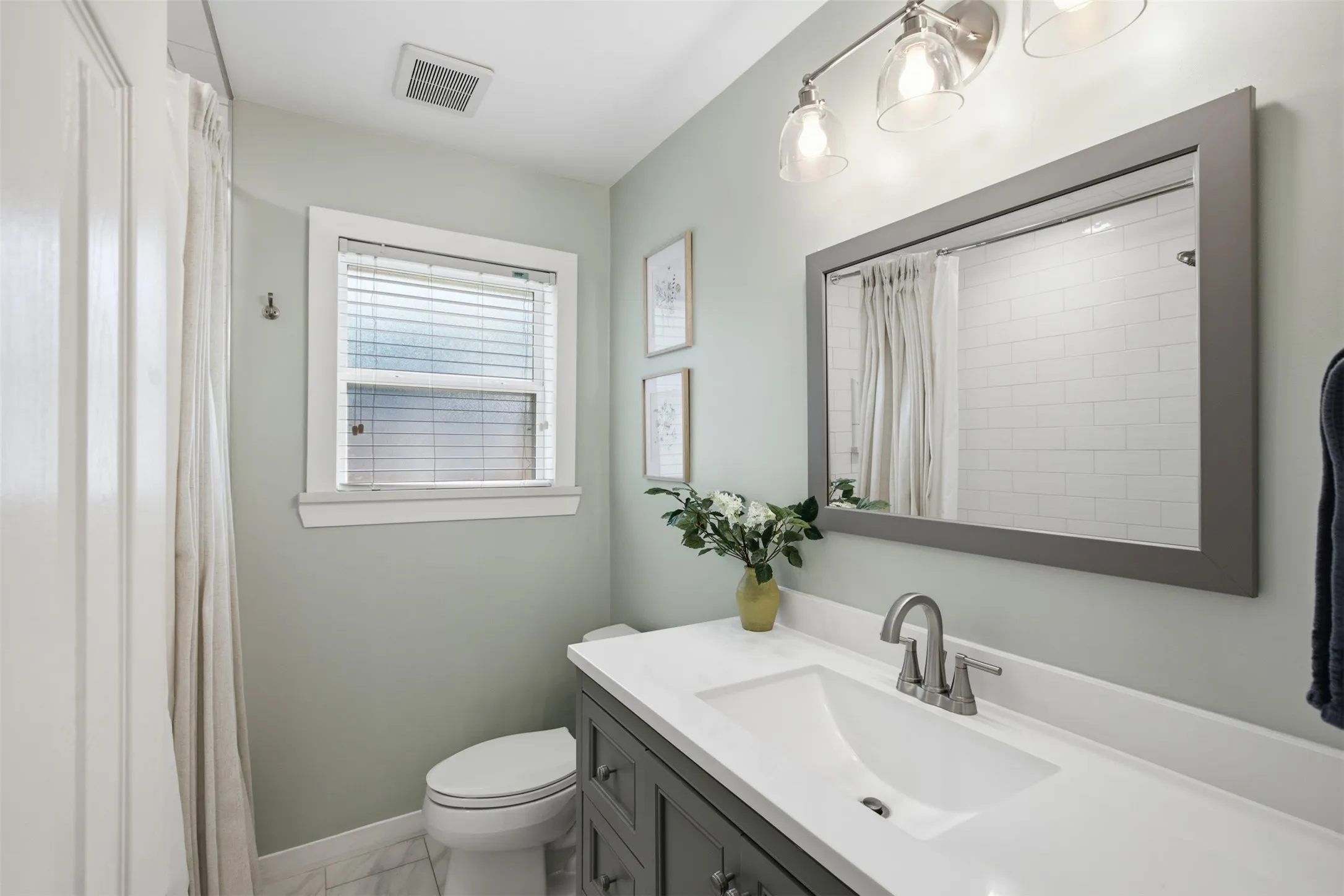 Single vanity with a white countertop and undermount sink, framed mirror, and chrome-finish light fixture