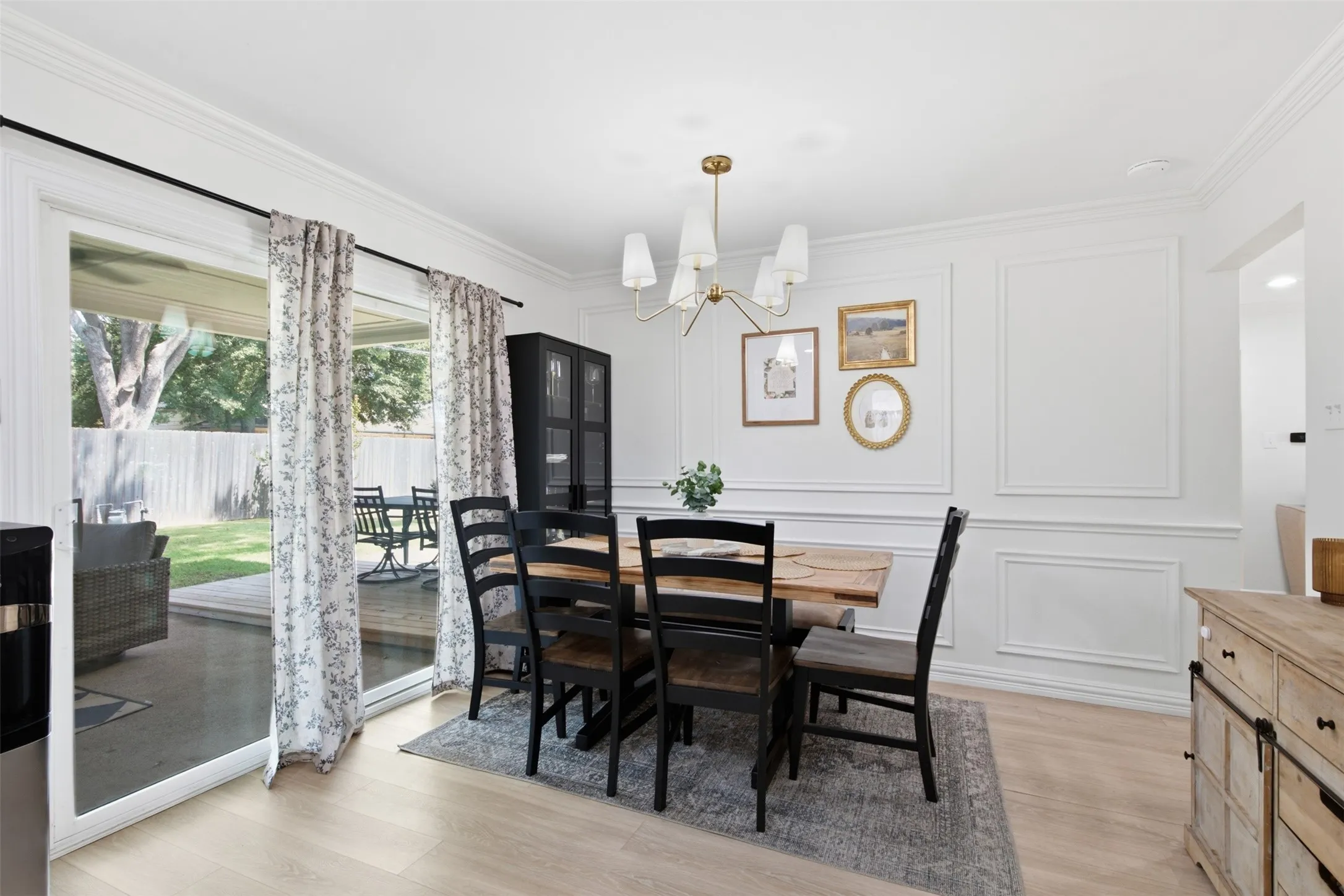 Light wood-finish flooring, crown molding, decorative wall molding, sliding glass door, and a modern chandelier