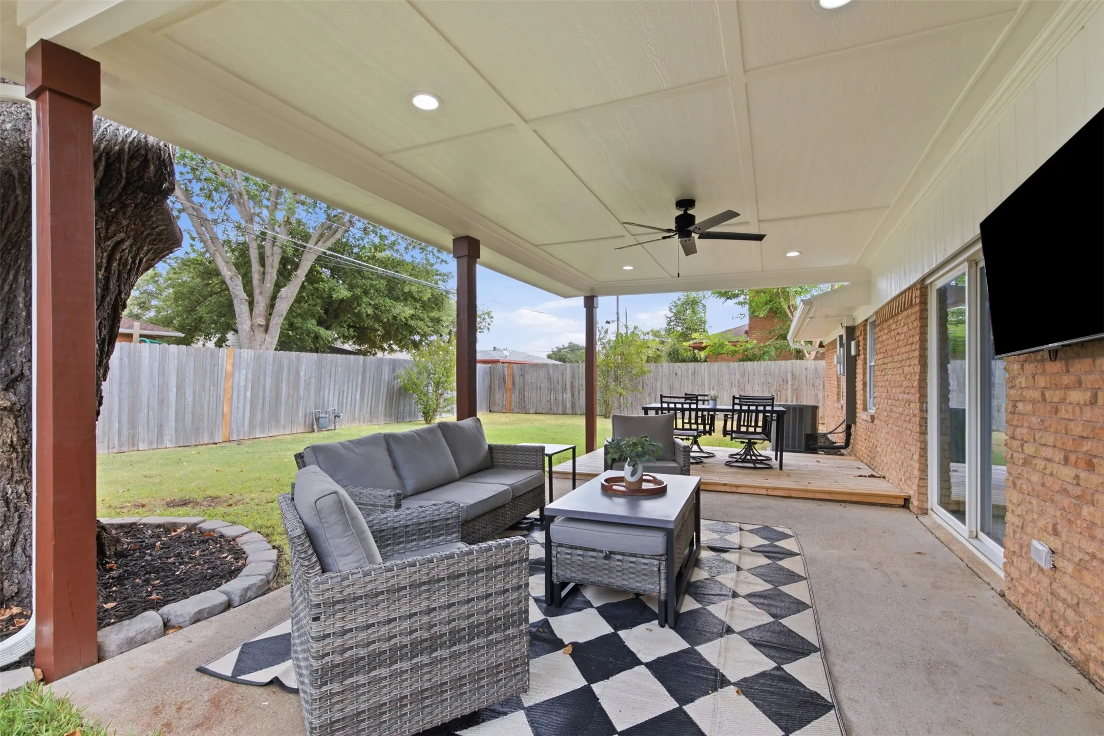 Expansive covered patio with recessed lighting and a ceiling fan, featuring a concrete pad and an elevated wood deck
