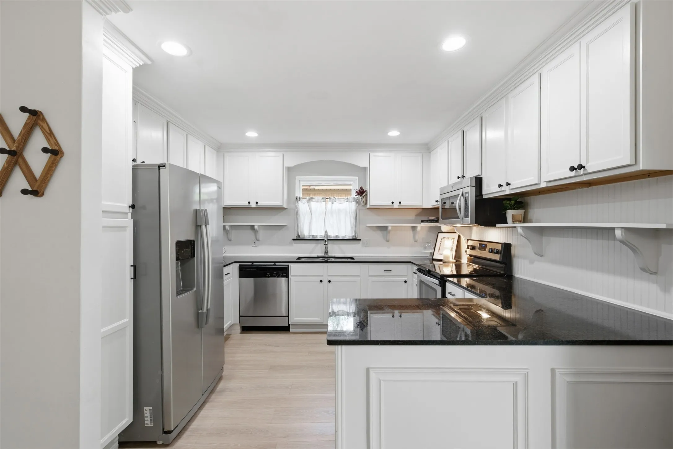 Kitchen featuring white shaker cabinetry, dark countertops, stainless steel appliances, and light wood-finish flooring