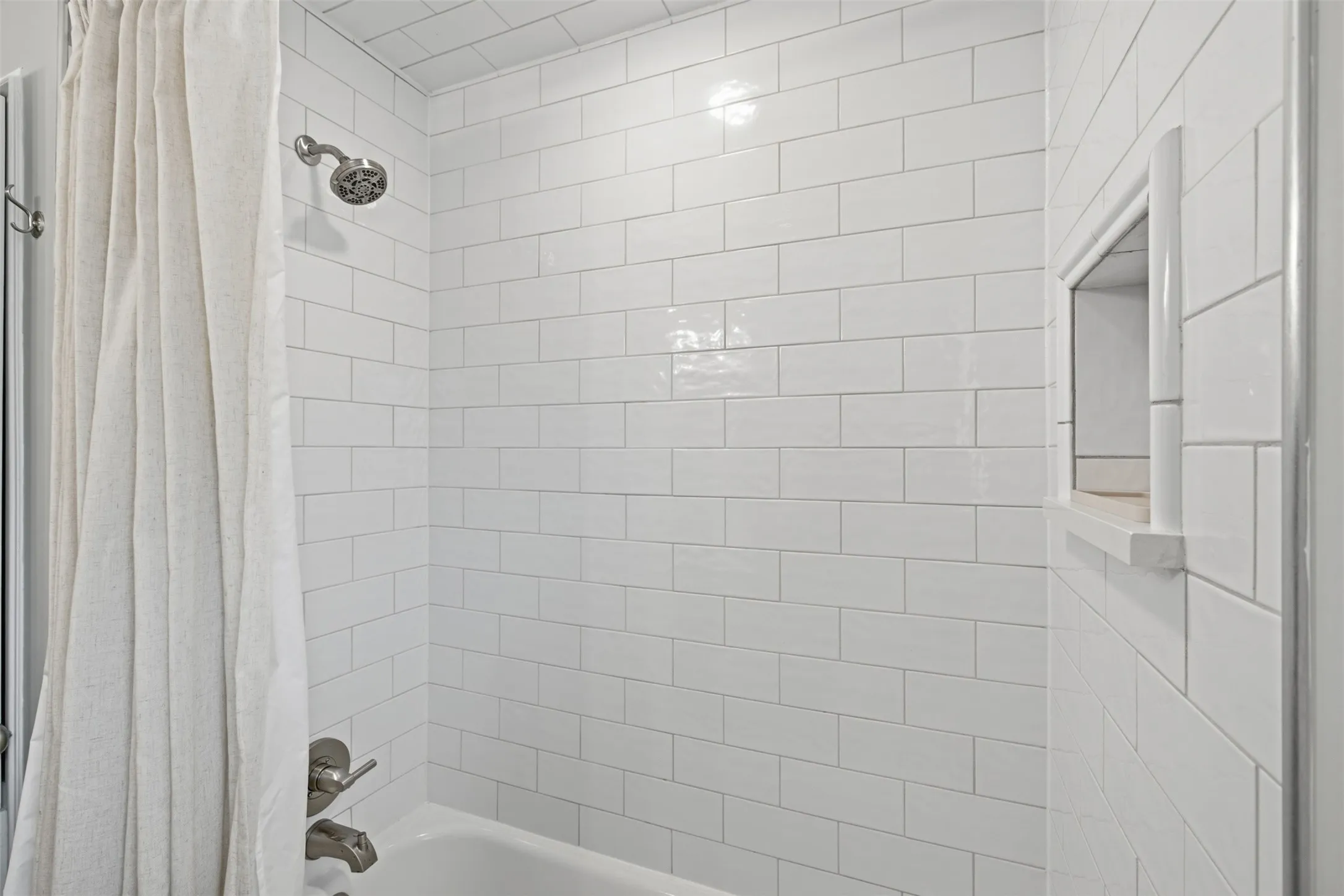 Bathtub with subway tile surround, brushed nickel showerhead, and integrated shelving niche