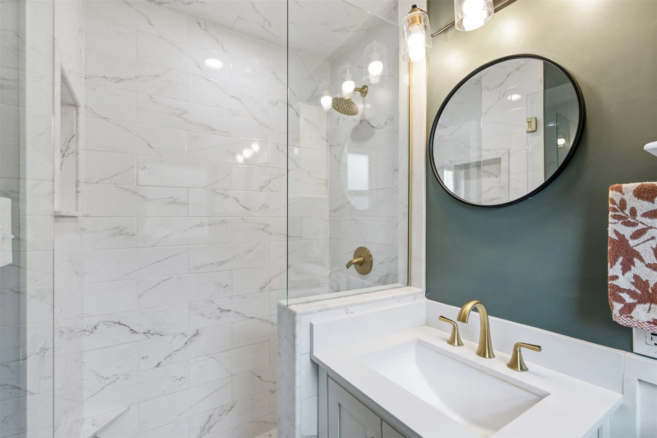 Glass-enclosed shower with white tiled walls, shower niche, and brass fixtures