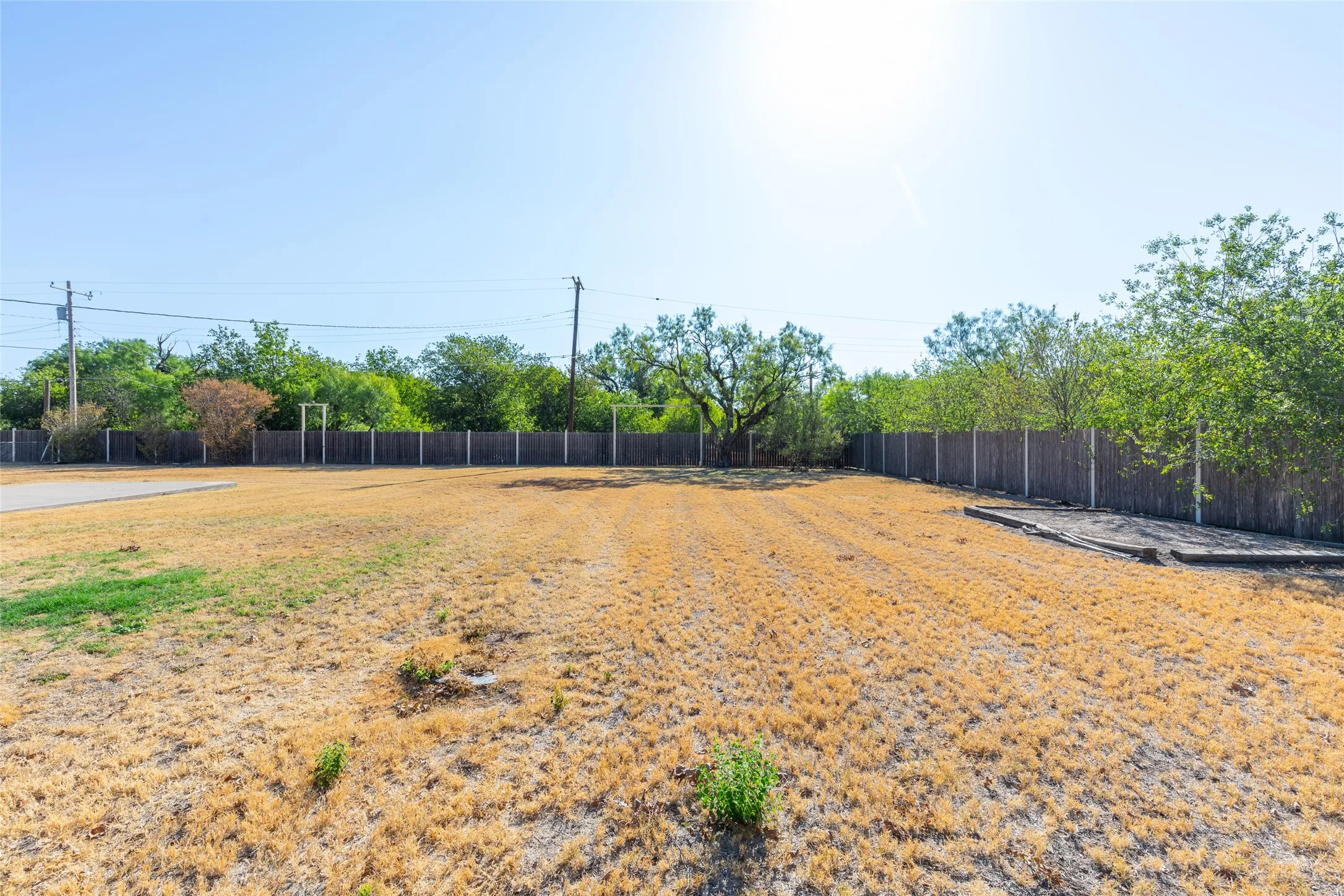 Expansive open lot with a partial paved surface and a perimeter fence