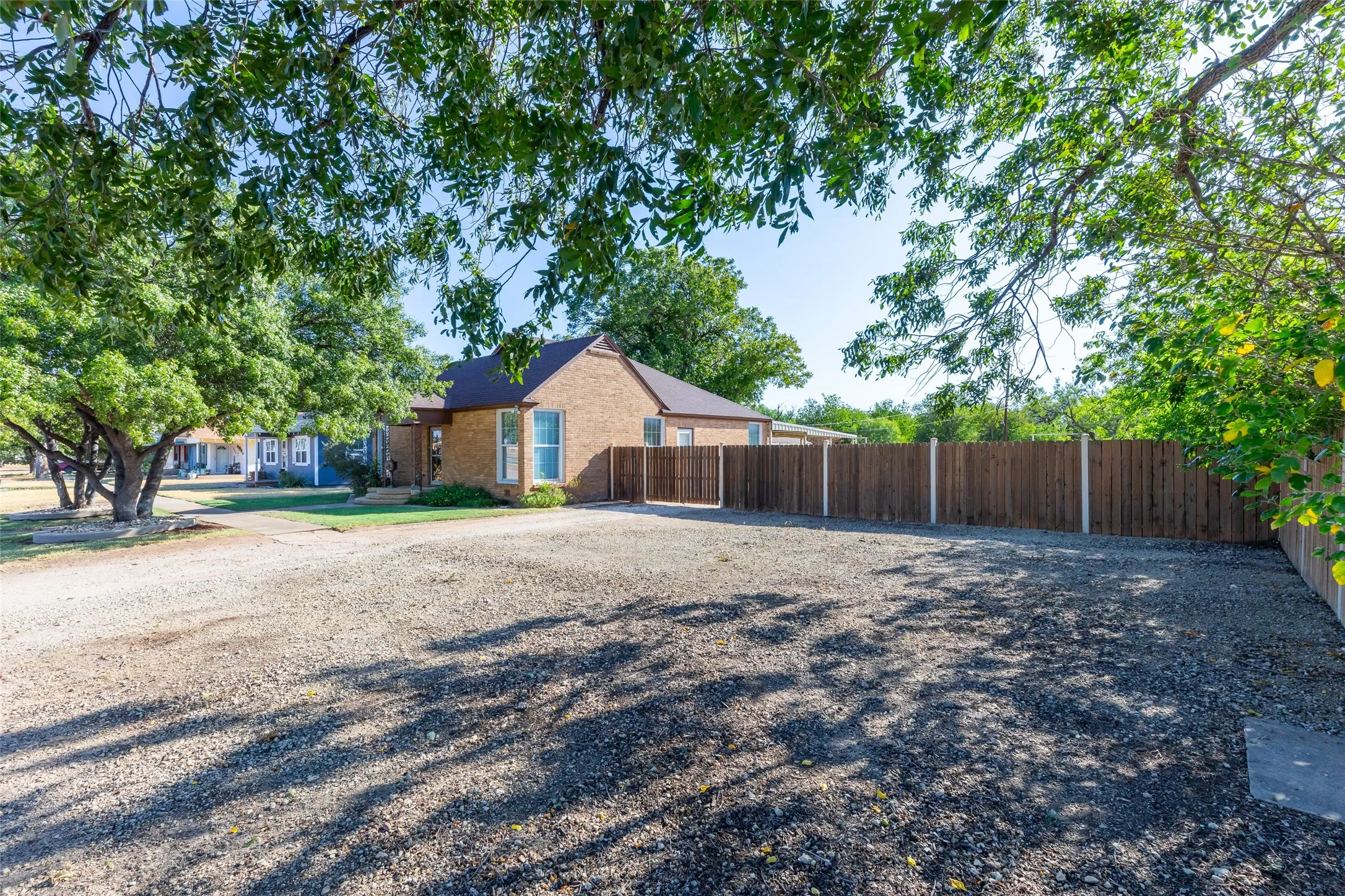 Extra large lot: Gravel parking area featuring a privacy fence and mature trees