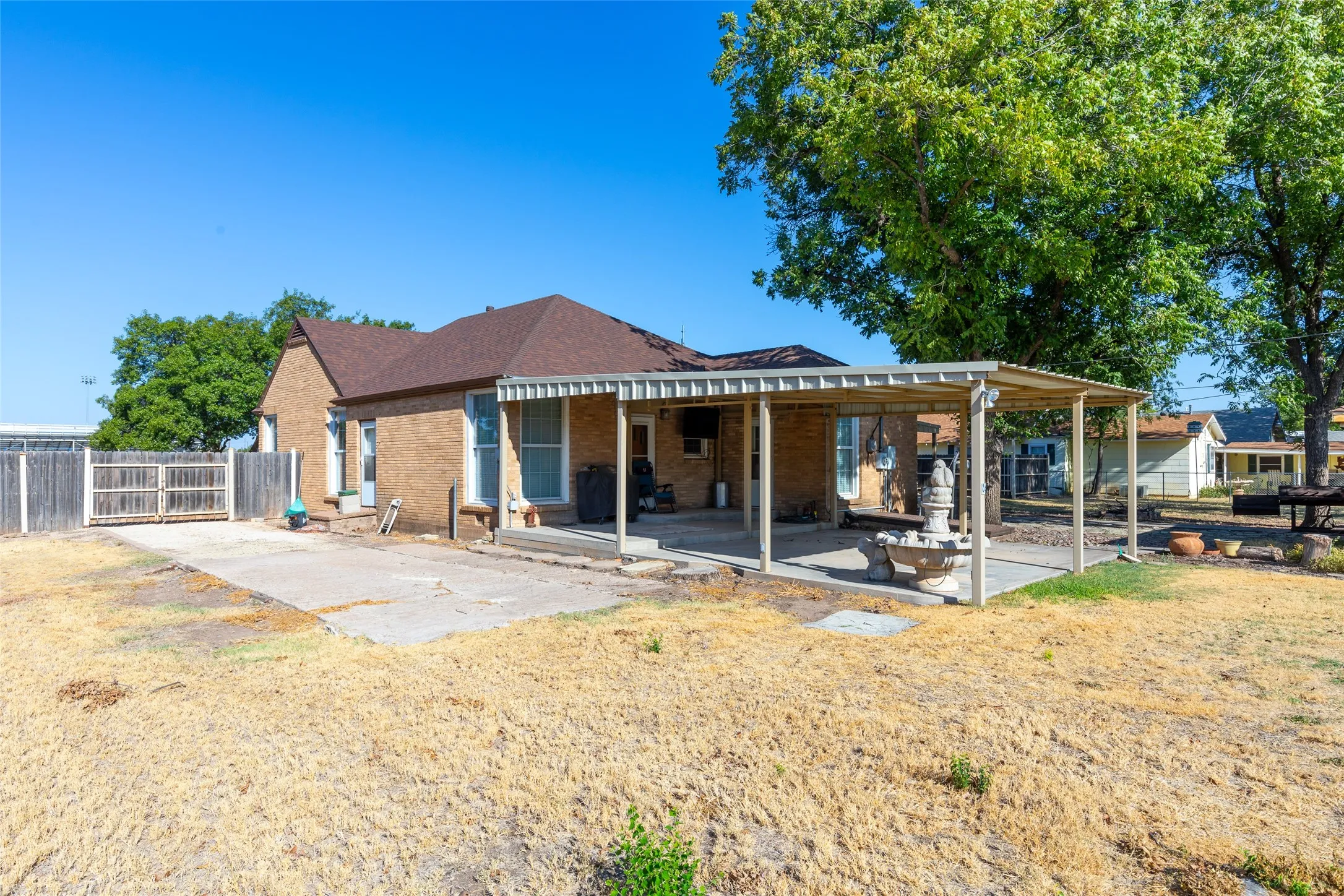 Brick exterior with a covered patio, mature trees, a fenced yard, and a concrete pad