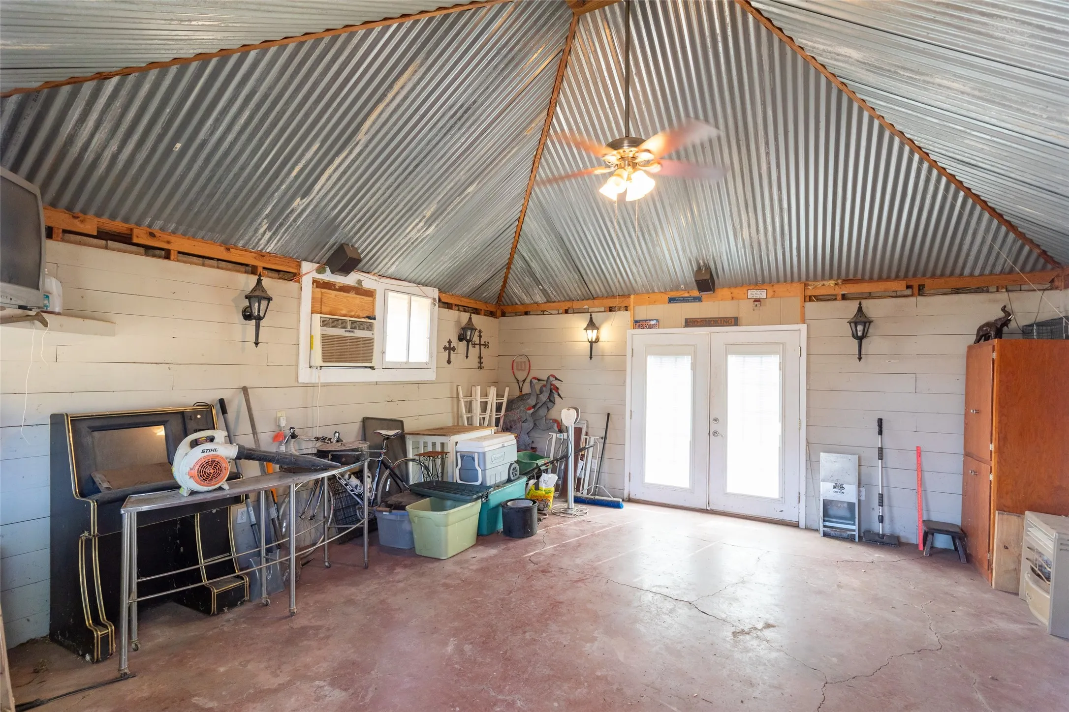 Corrugated metal vaulted ceiling with exposed wood beams, dual pane windows, and a ceiling fan with integrated lighting