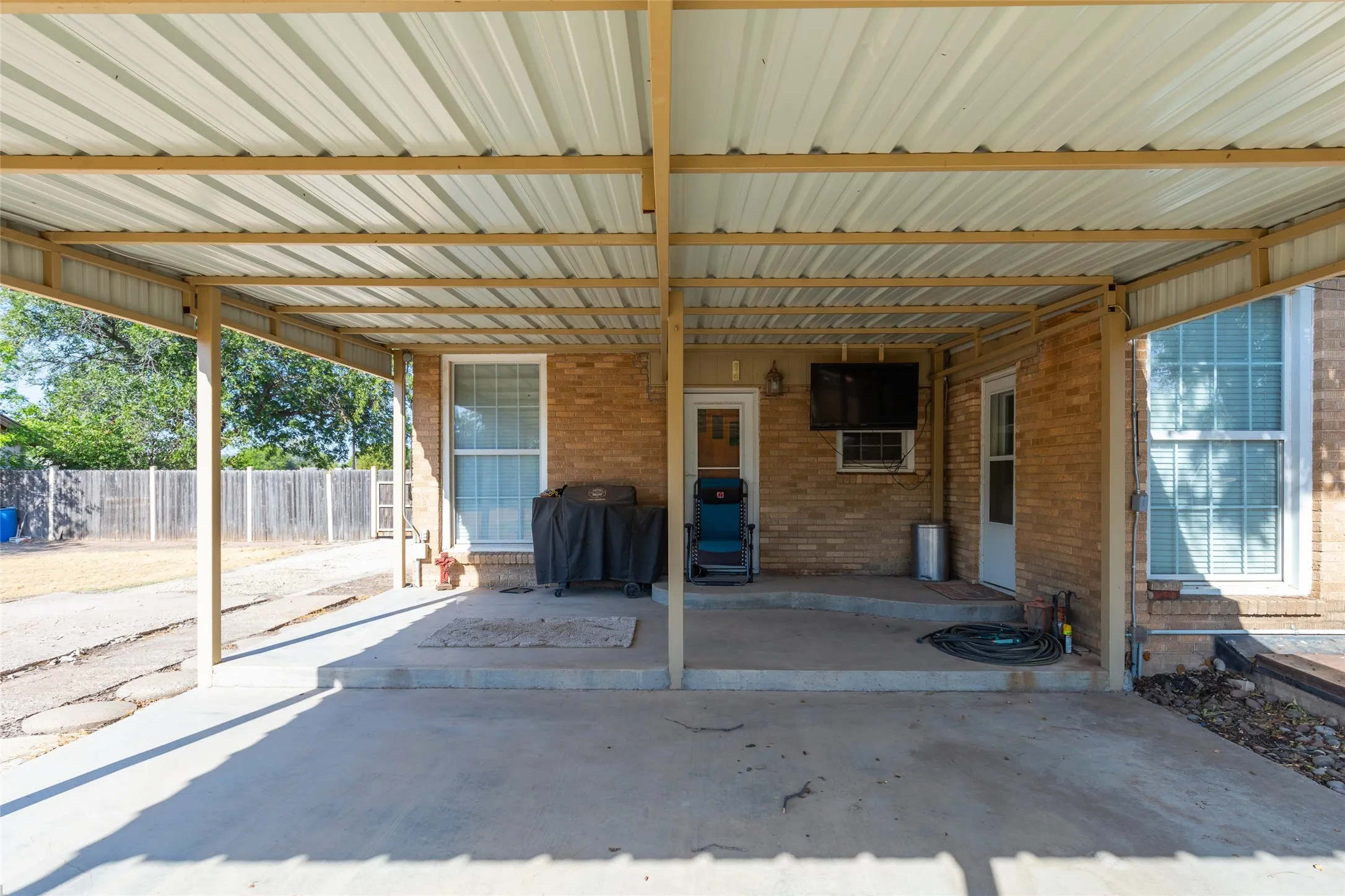 Expansive covered patio featuring a metal roof structure, concrete flooring, and brick exterior walls