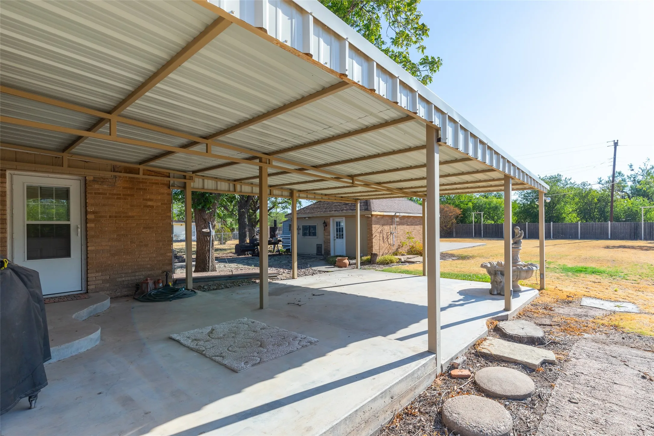 Covered concrete patio with metal roof structure, brick exterior, and stone stepping path