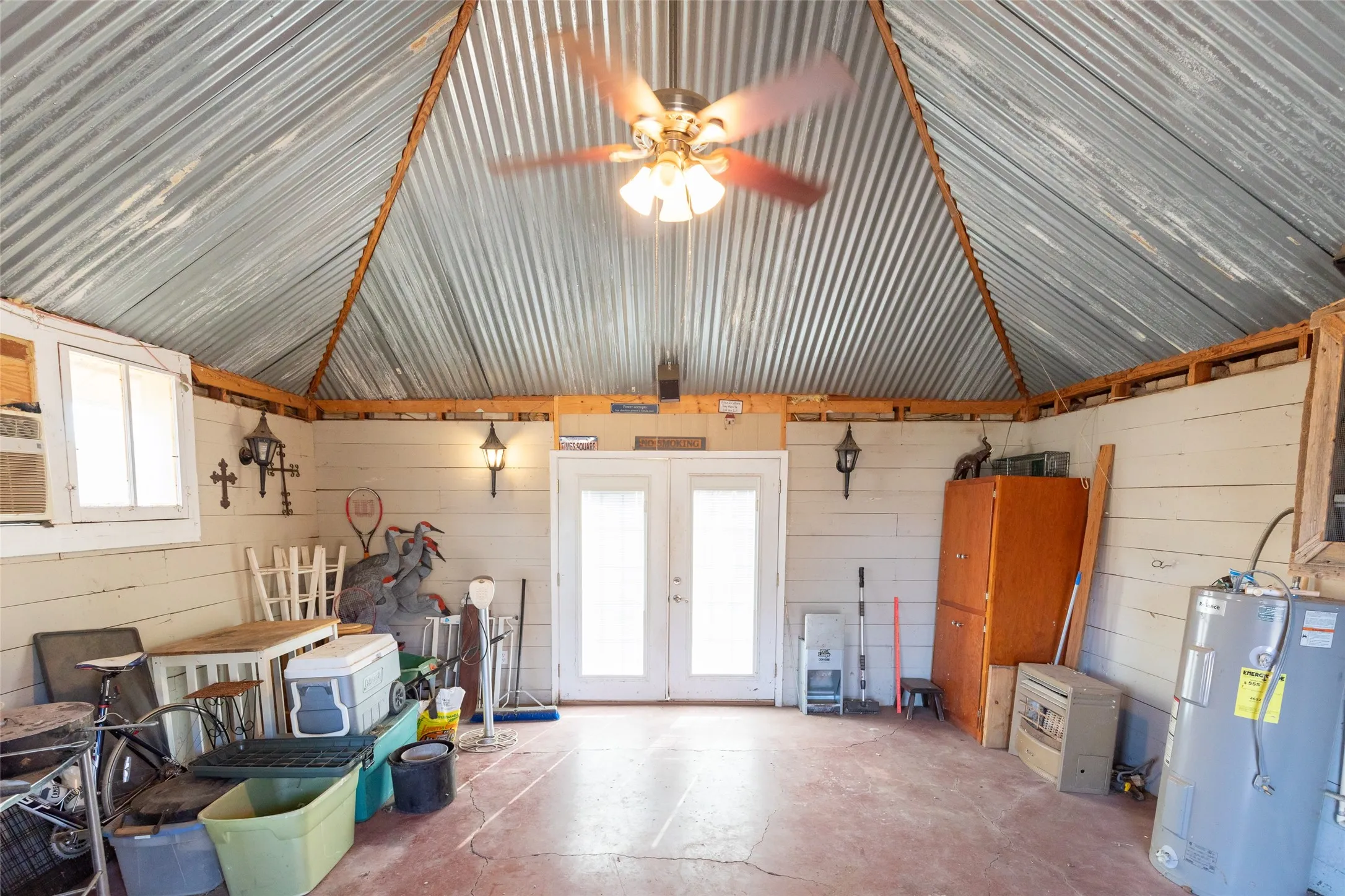 Corrugated metal vaulted ceiling with exposed wood beams, dual pane windows, and a ceiling fan with integrated lighting