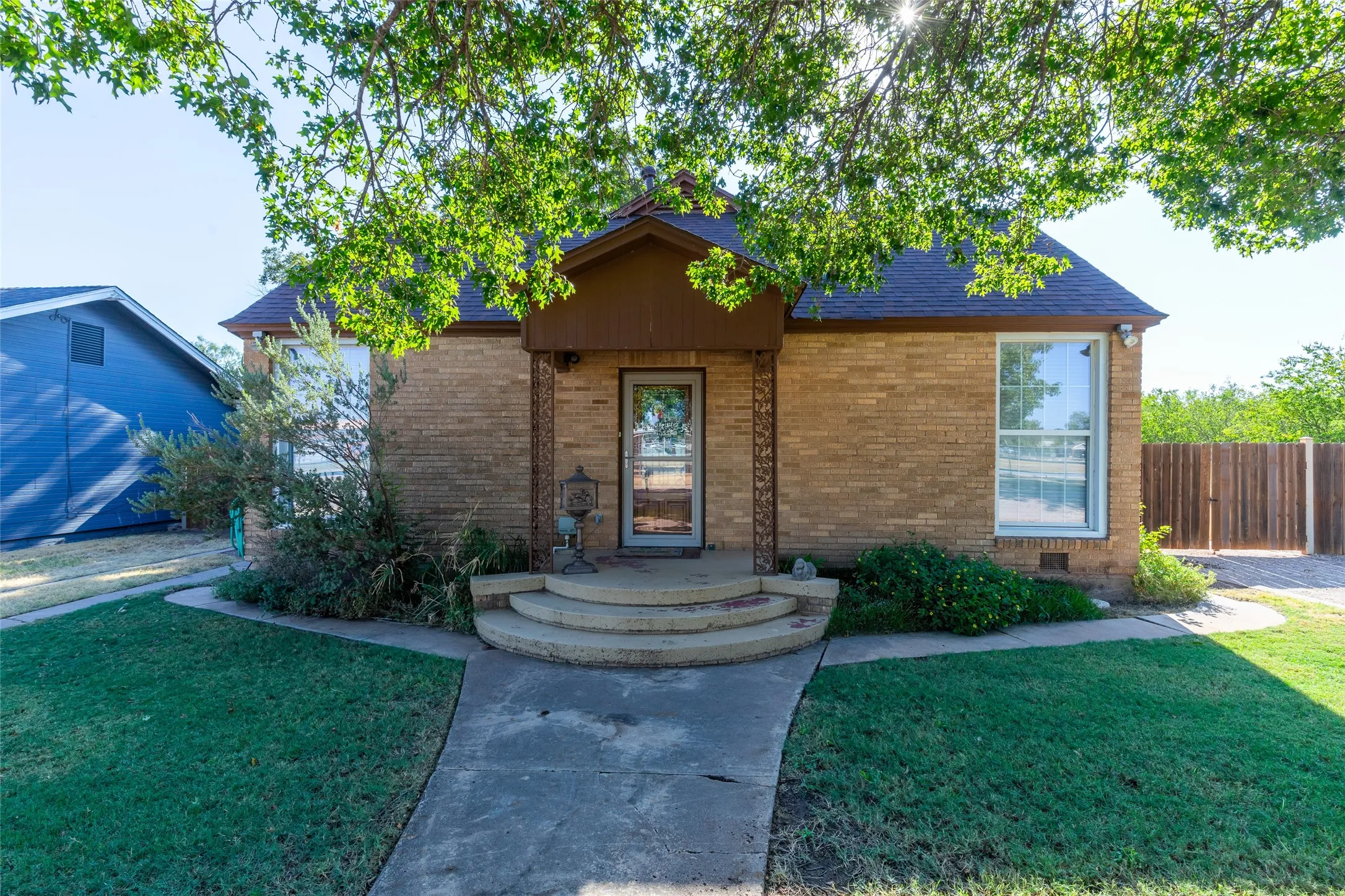 Brick facade residence with a dark shingle roof, established landscaping, and a privacy fence