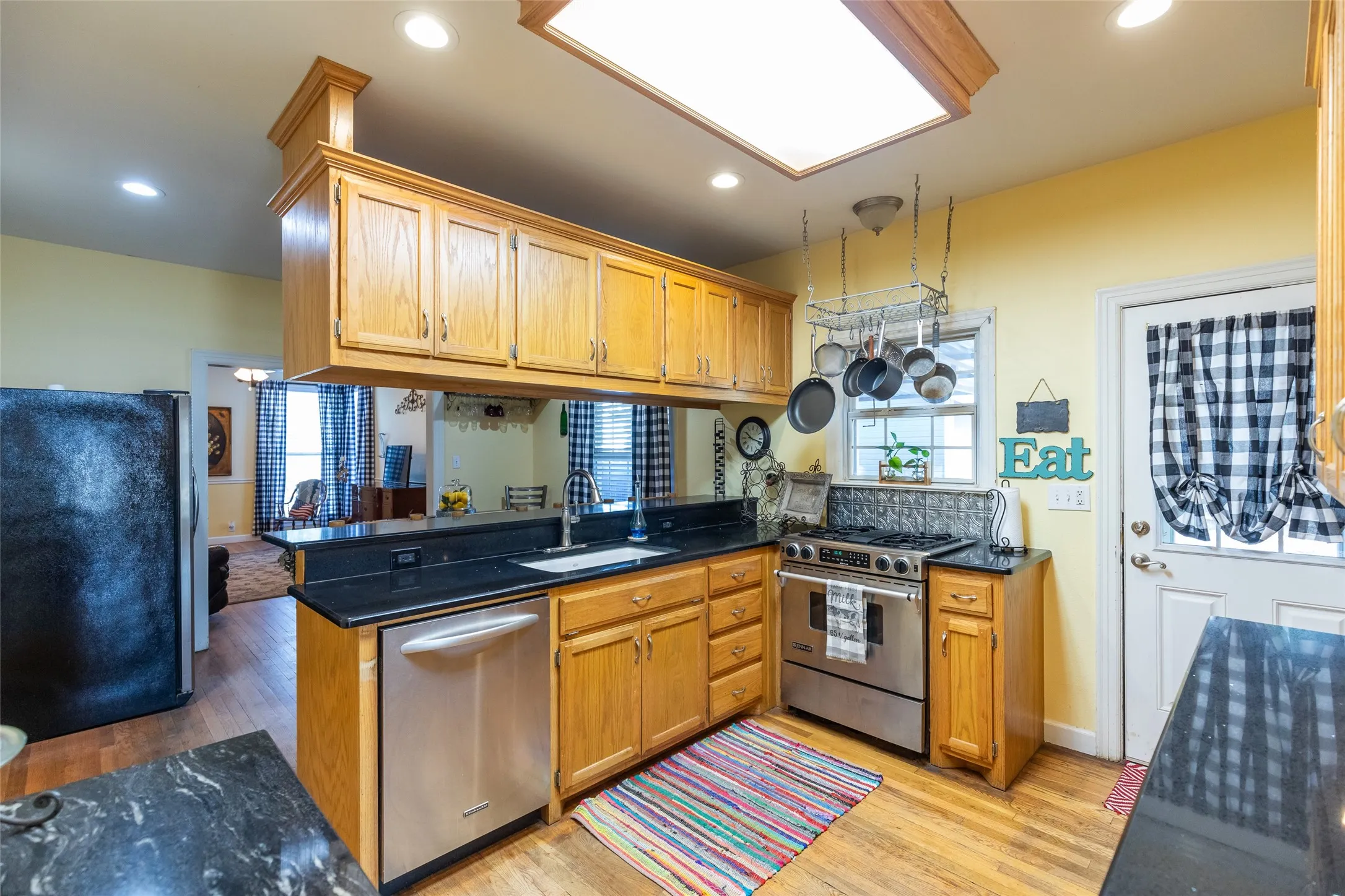 Kitchen featuring wood-finish cabinetry, black countertops, stainless steel appliances, and wood-finish flooring