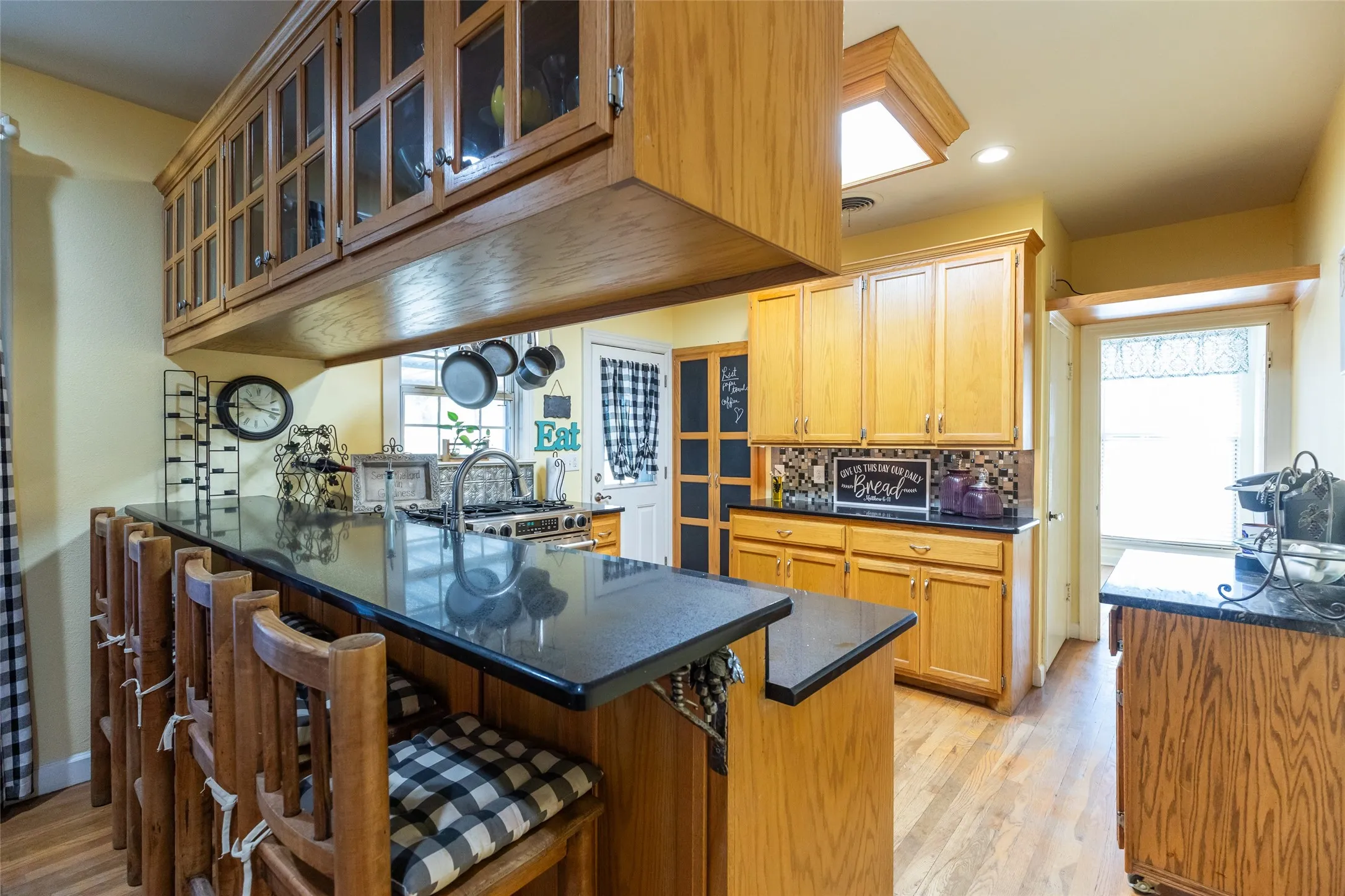 Wood-finish cabinetry, black countertops, wood-finish flooring, recessed lighting, and a skylight
