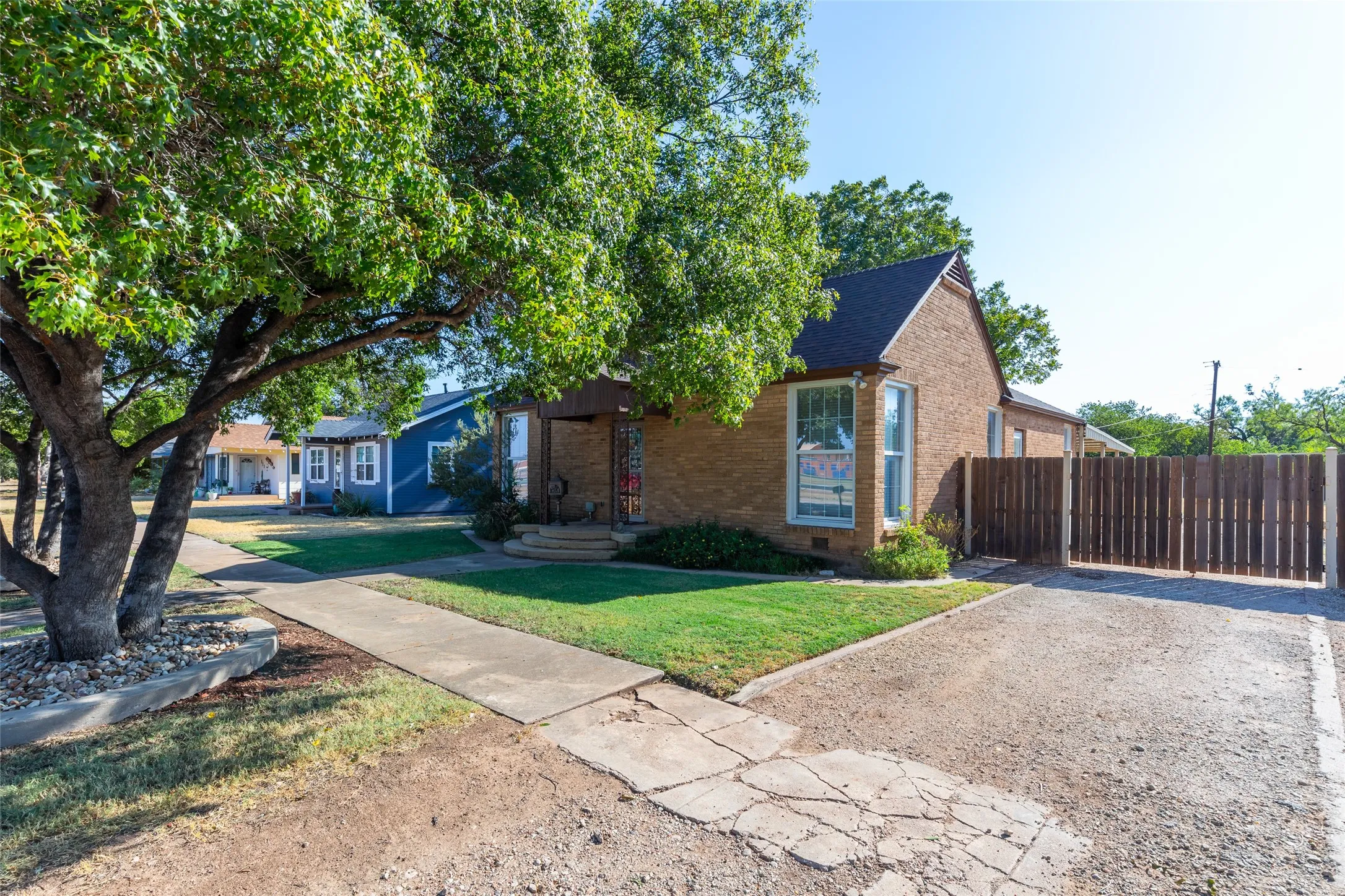 Brick exterior with a dark-pitched roof, featuring mature trees, a manicured lawn, and a privacy fence