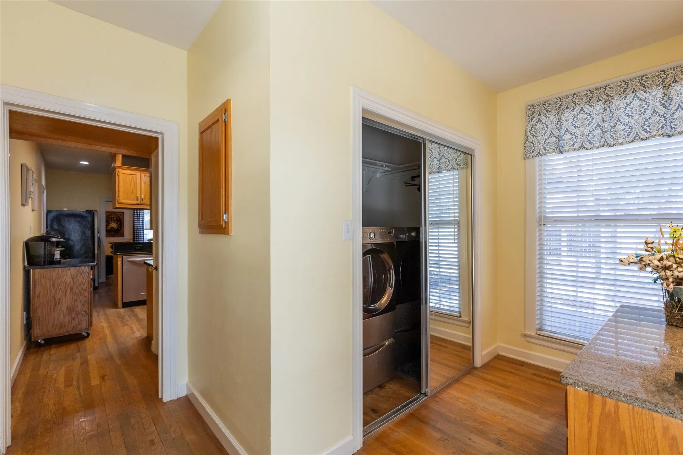 Wood-finish flooring throughout, with a window featuring blinds and a patterned valance