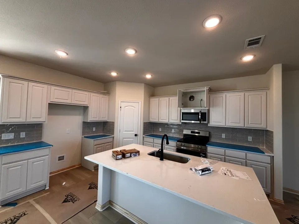 Kitchen featuring a large island with sink, white cabinetry, integrated microwave, and stainless steel range