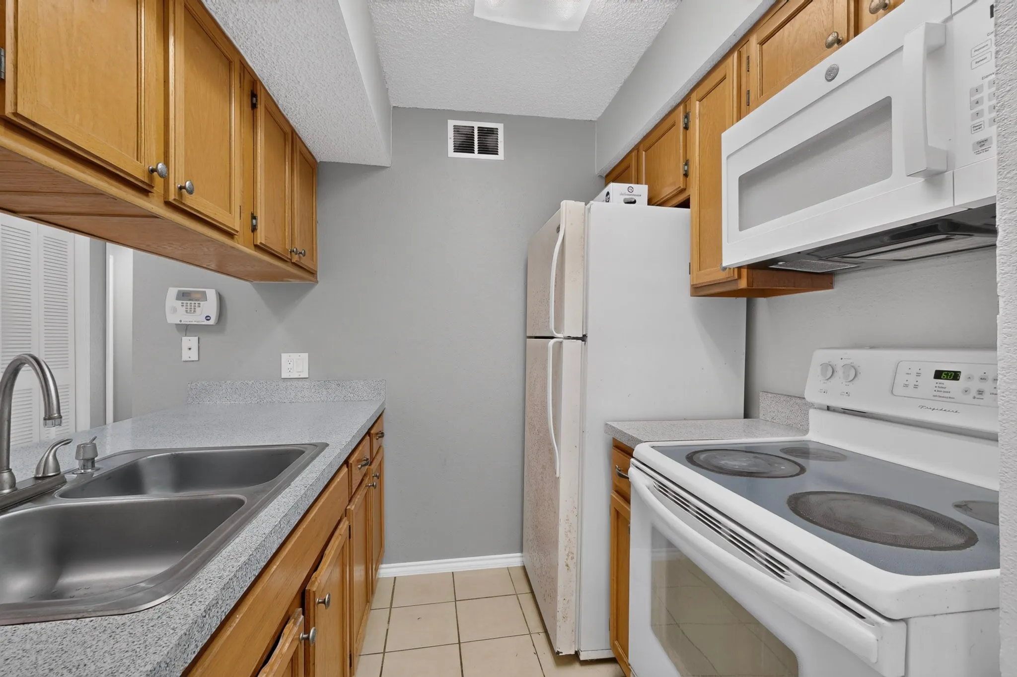 Kitchen featuring wood cabinetry, a double basin stainless steel sink, light-toned countertops, and tile flooring