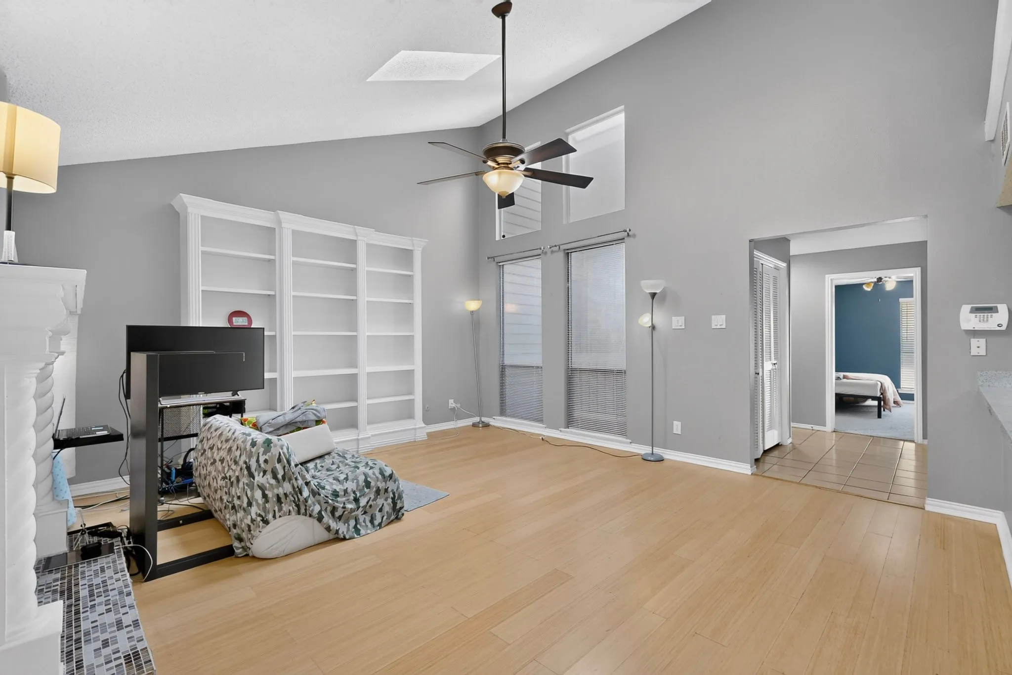 Vaulted ceiling with a ceiling fan, recessed windows, wood-finish flooring, built-in shelving, and a tiled fireplace surround