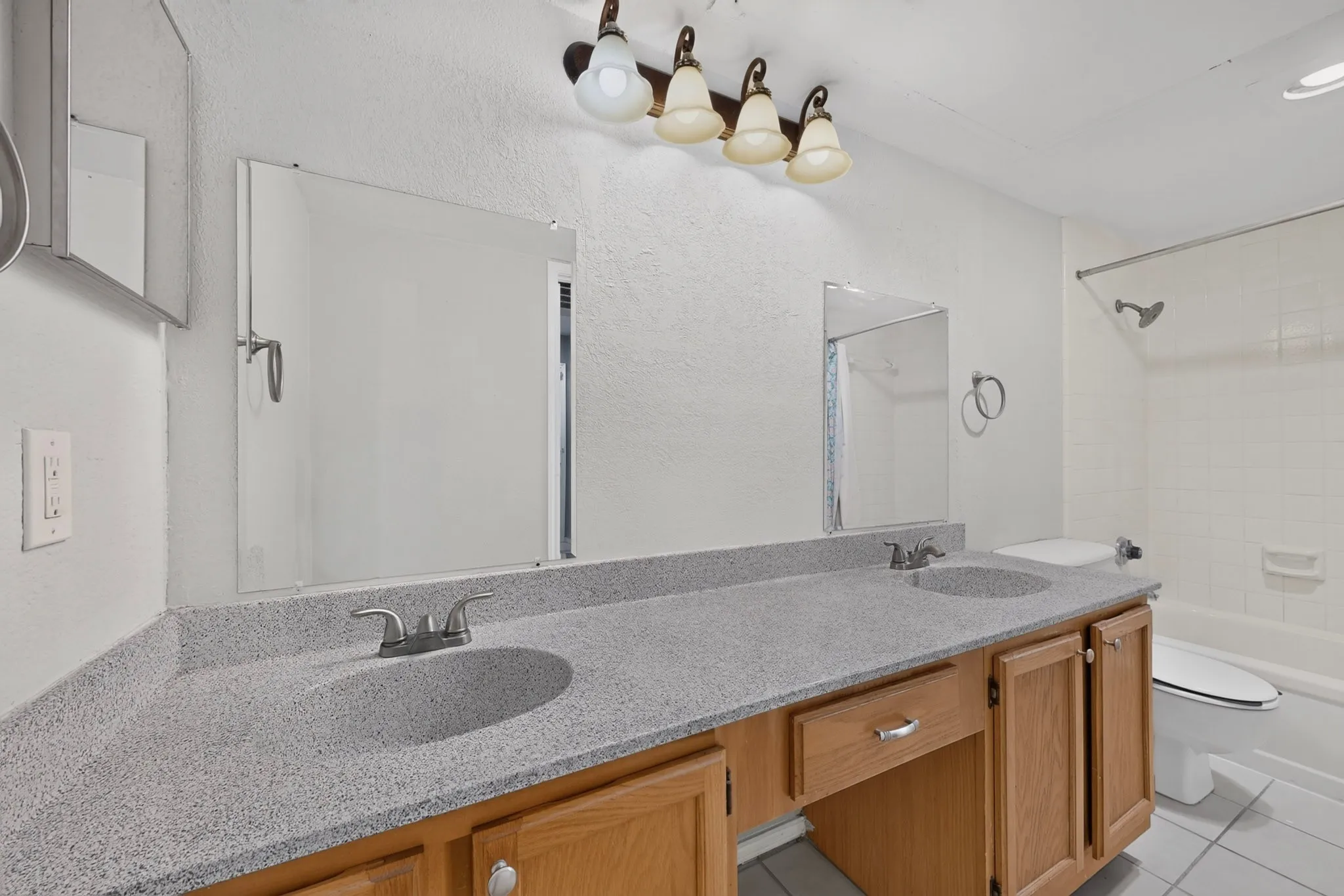 Double vanity with integrated sinks, light-toned countertop, wood-finish cabinetry, and a full-size bathtub with shower