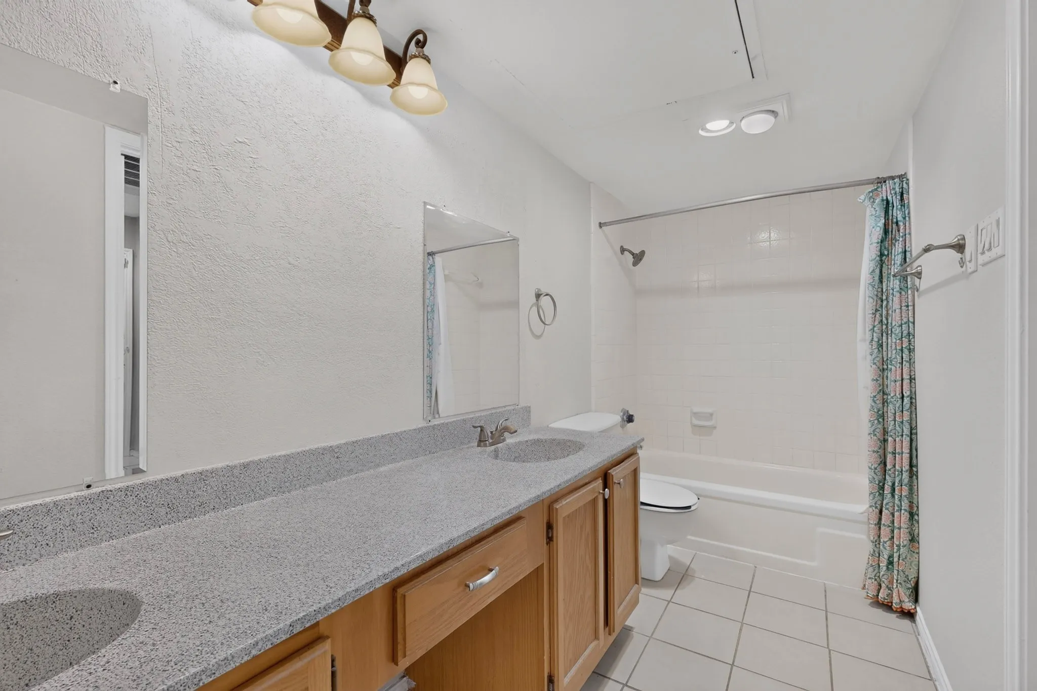 Double vanity with integrated sinks and wood-finish cabinetry, tile flooring, and a shower-tub combination