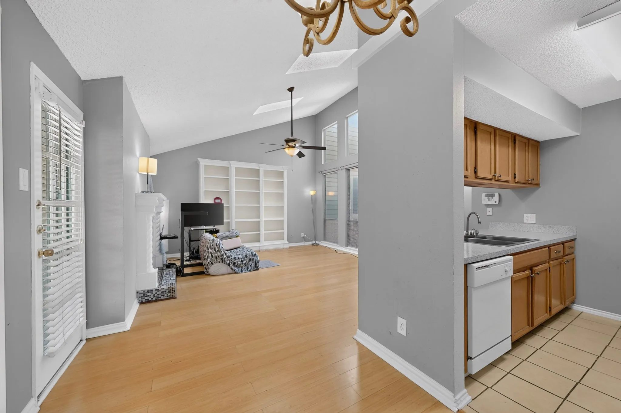 Living area with vaulted ceiling, wood-finish flooring, built-in shelving, fireplace, and integrated kitchen with wood cabinetry