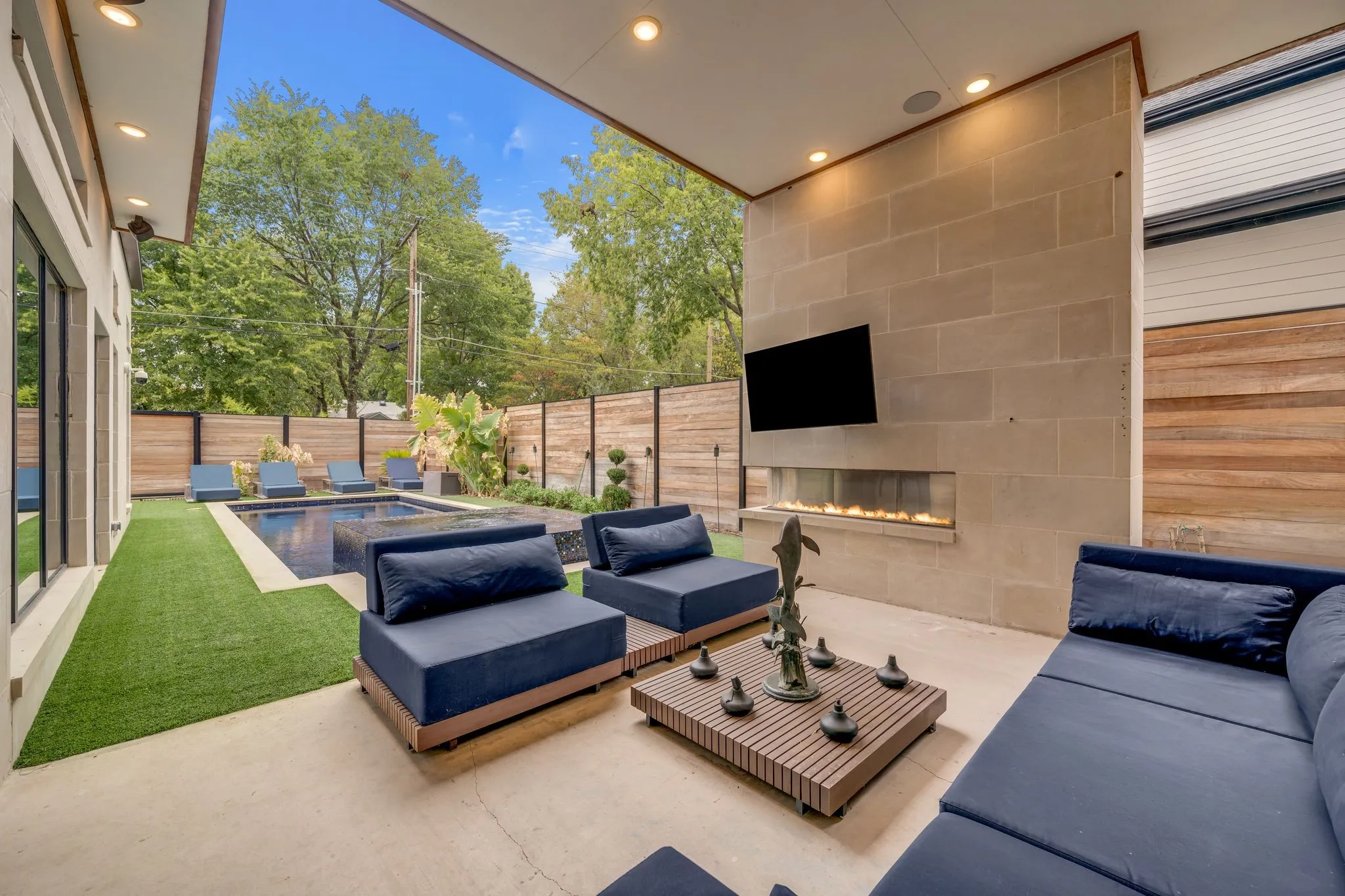 Covered outdoor living space featuring recessed lighting, a stone-clad accent wall with a built-in linear fireplace, and a television mount