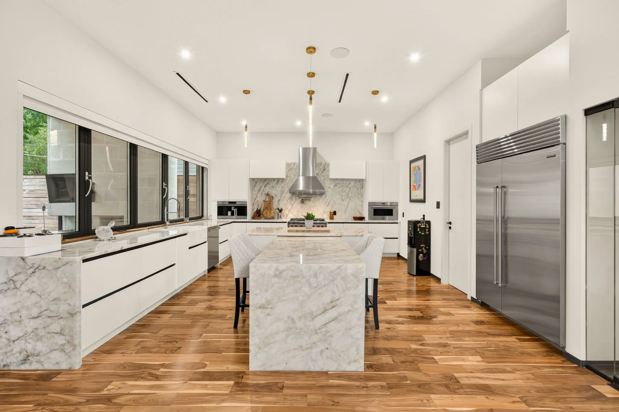 Spacious kitchen with a large stone-finish island, wood-finish flooring, and integrated stainless steel appliances