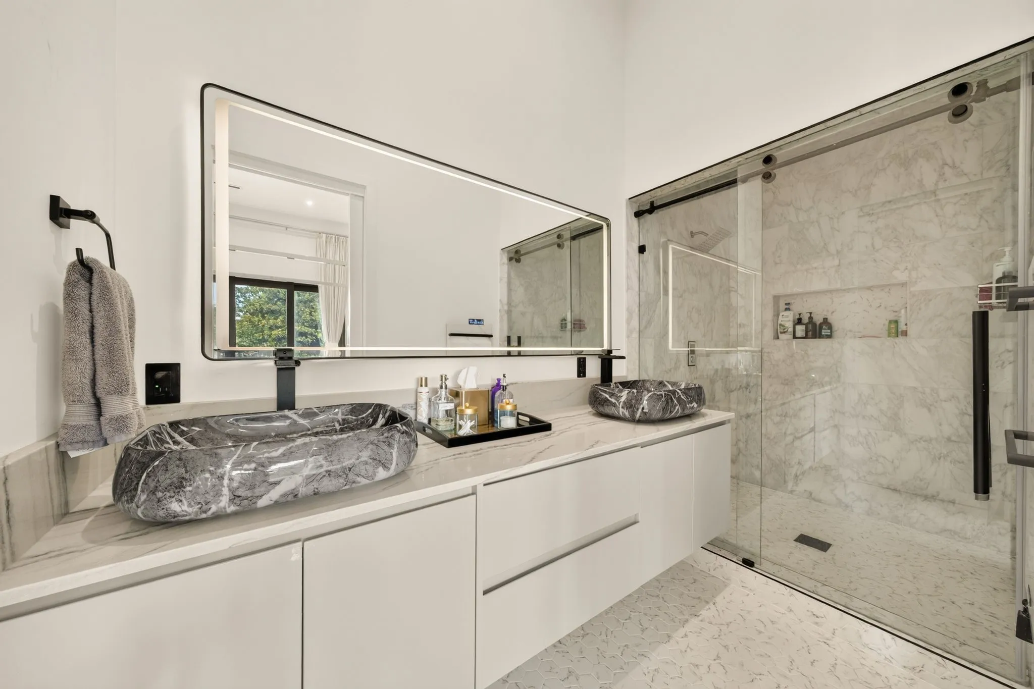 Dual vanity with stone vessel sinks, large illuminated mirror, frameless glass shower enclosure, and full-height tiled shower walls