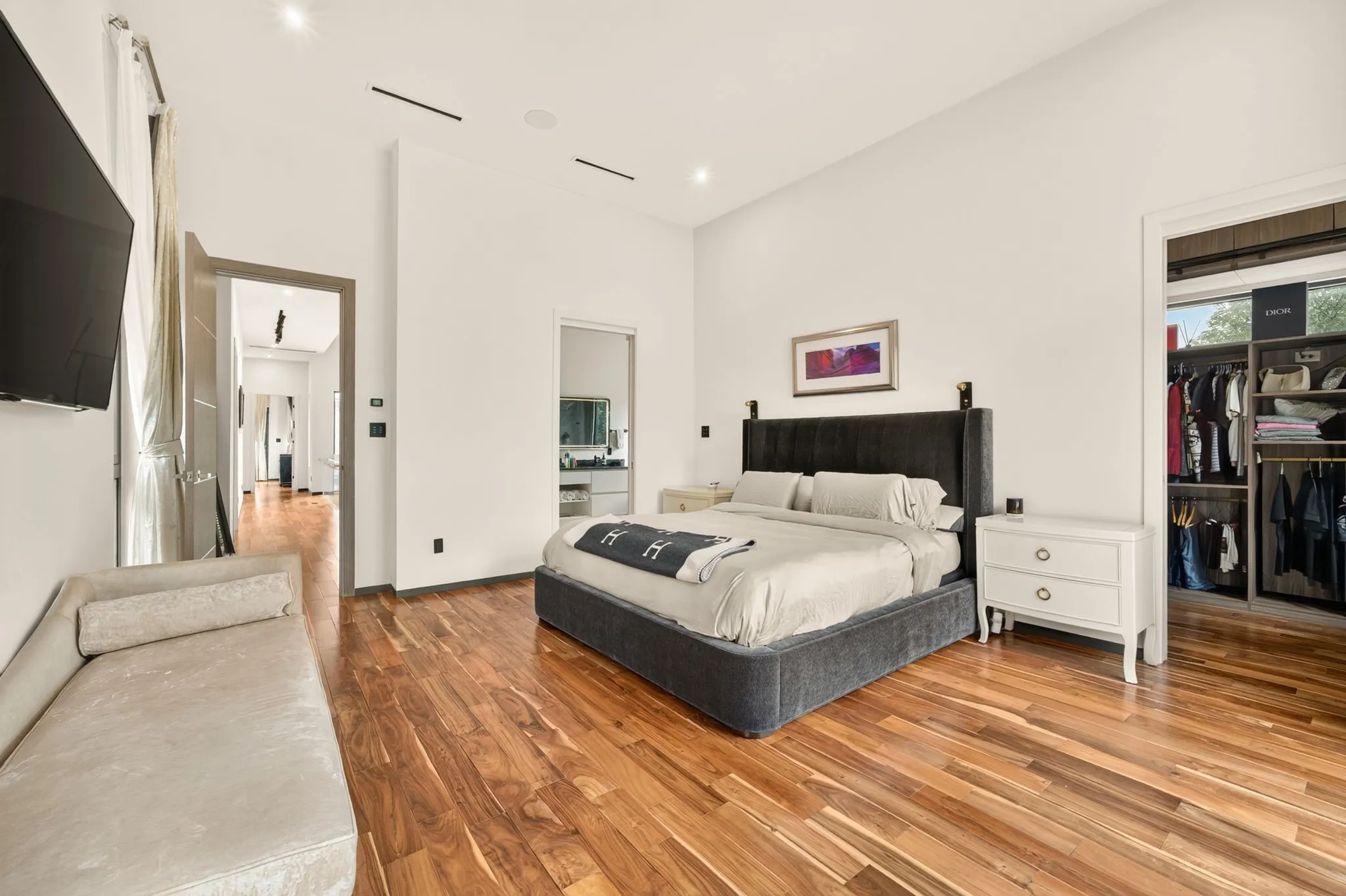 Hardwood flooring, high ceilings with recessed lighting, integrated wall-mounted television, and an open-concept closet with built-in shelving