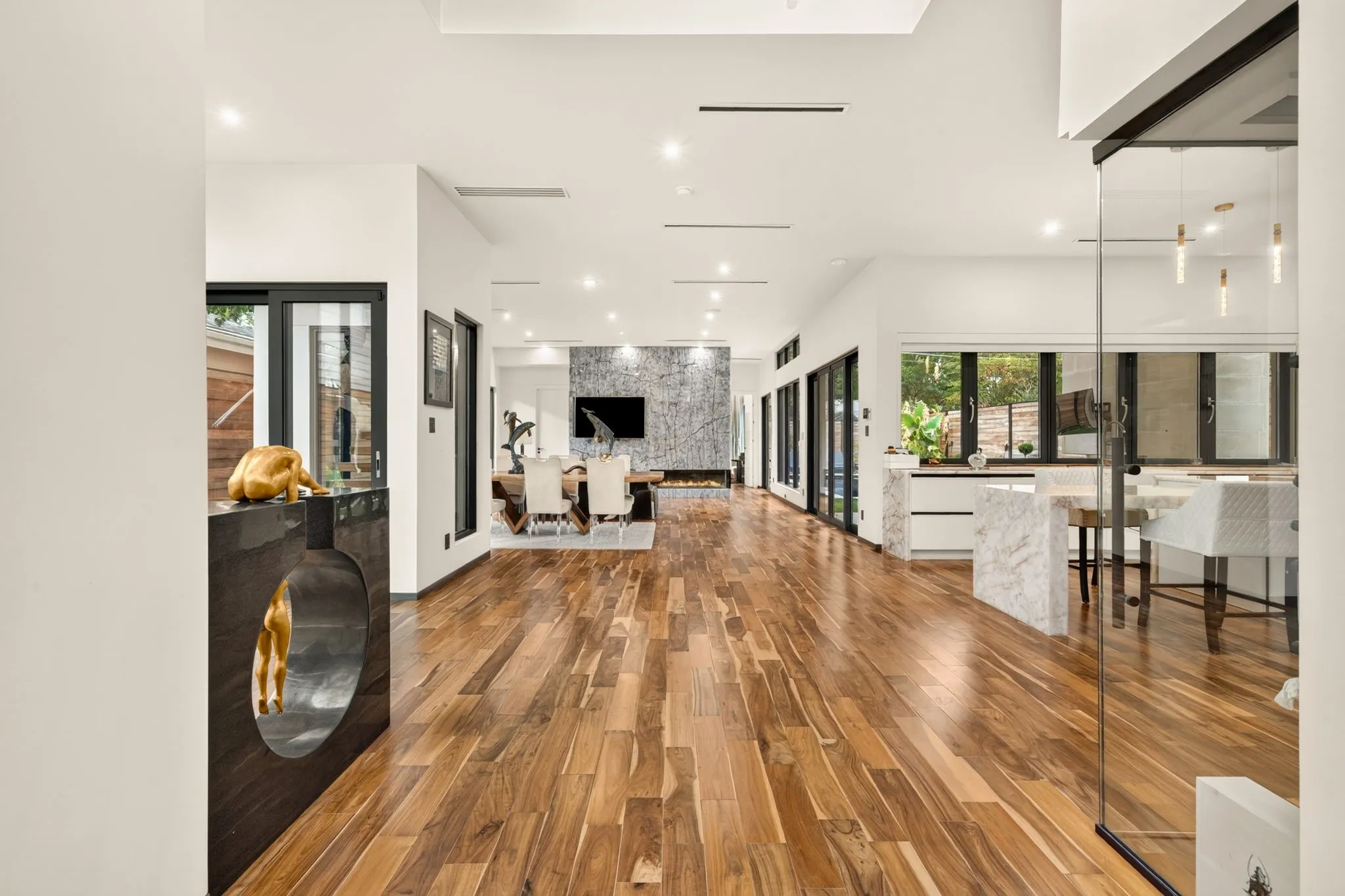 Warm-toned wood flooring extending throughout, recessed lighting, and a kitchen featuring a waterfall island with an integrated breakfast bar