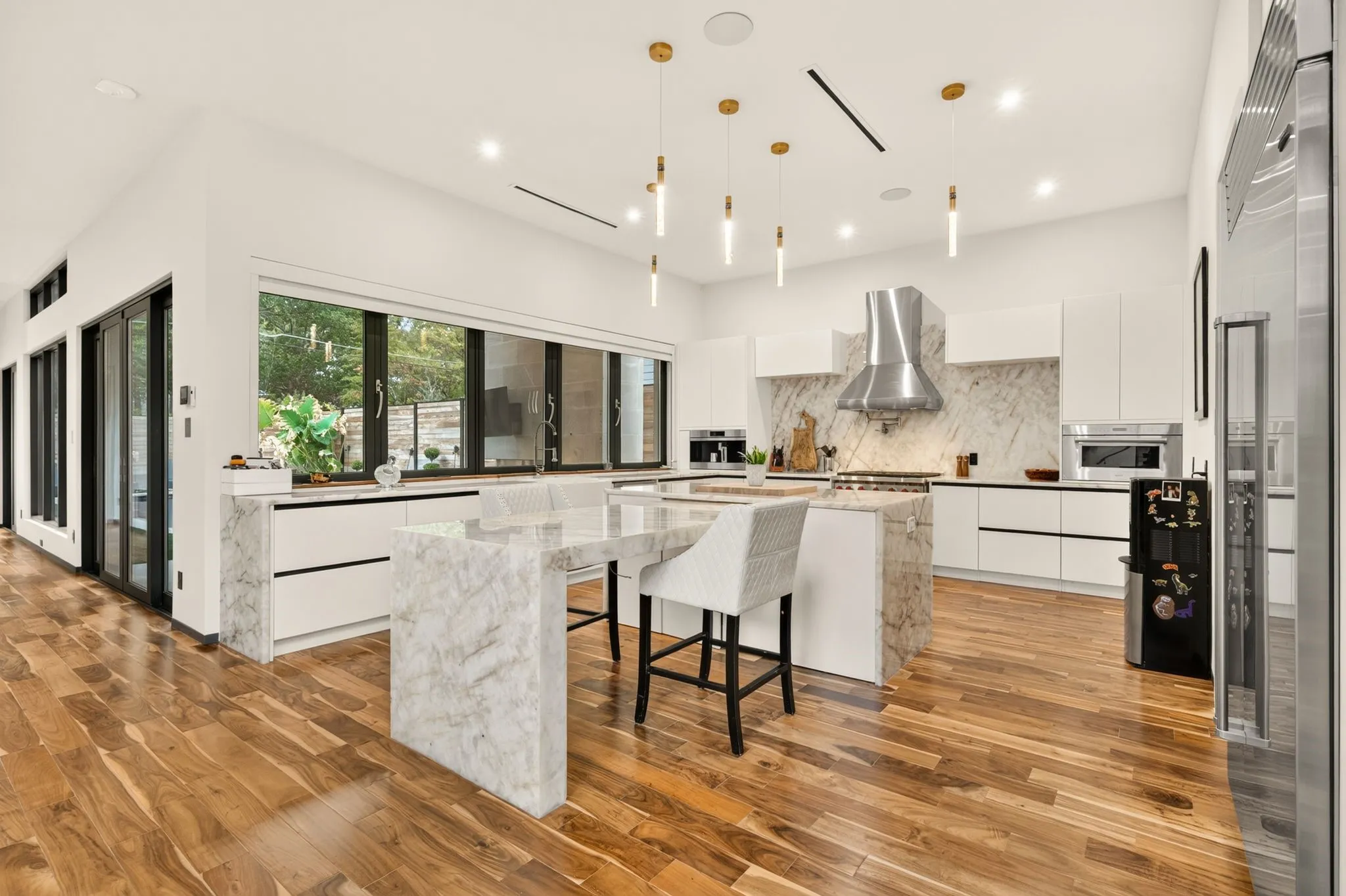 Gourmet kitchen featuring a waterfall island, integrated appliances, hardwood flooring, and abundant natural light