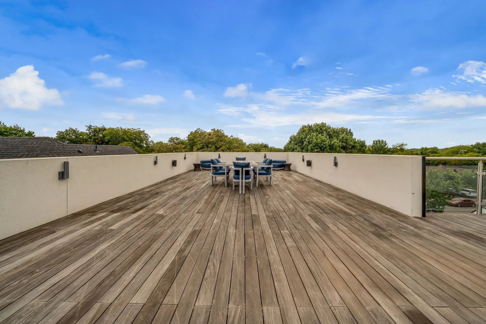 Expansive roof deck featuring wood-finish flooring, a white perimeter wall, and modern wall-mounted lighting fixtures