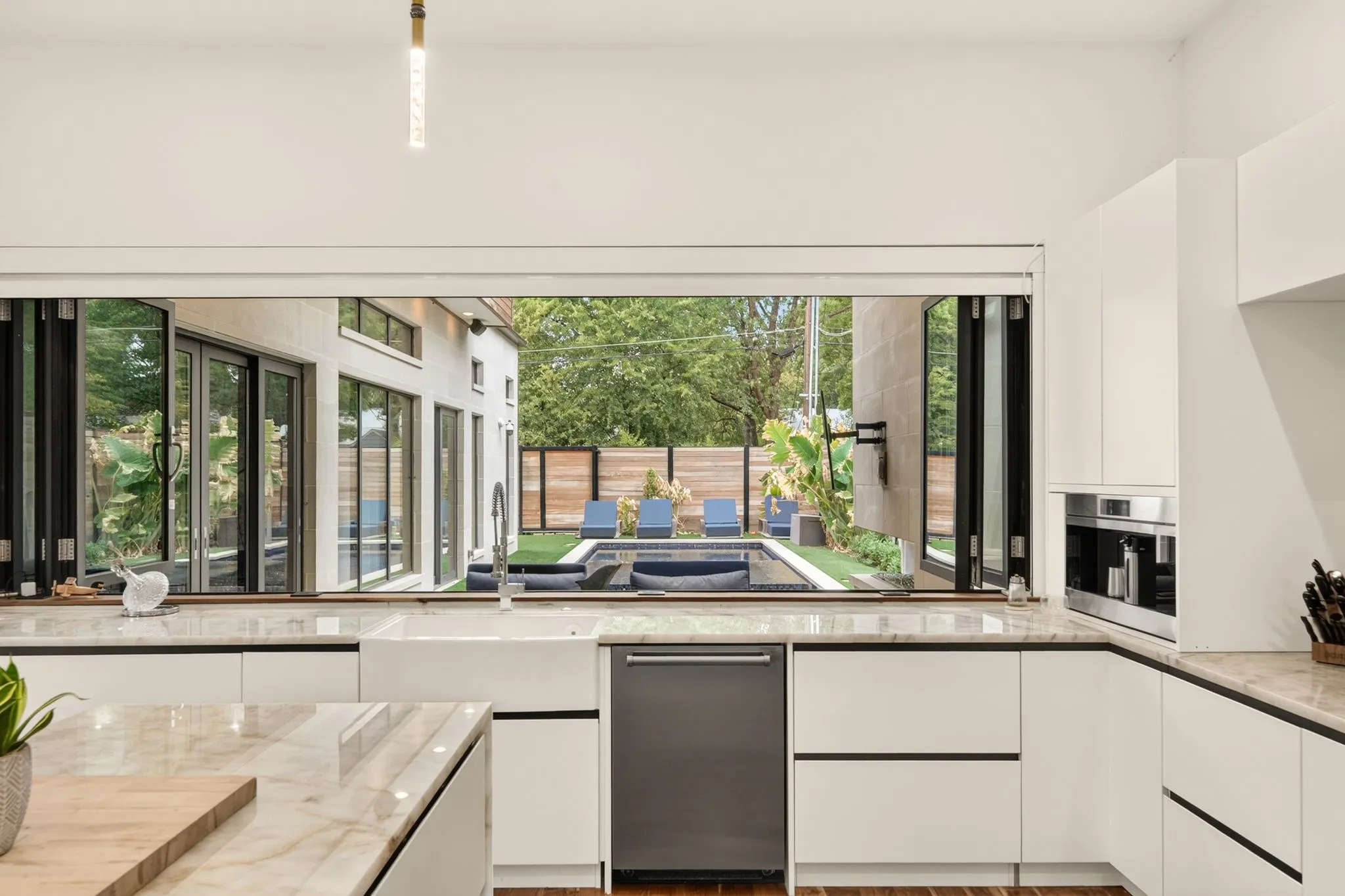 Modern kitchen featuring white cabinetry, stone countertops, a farmhouse sink, and integrated stainless steel appliances