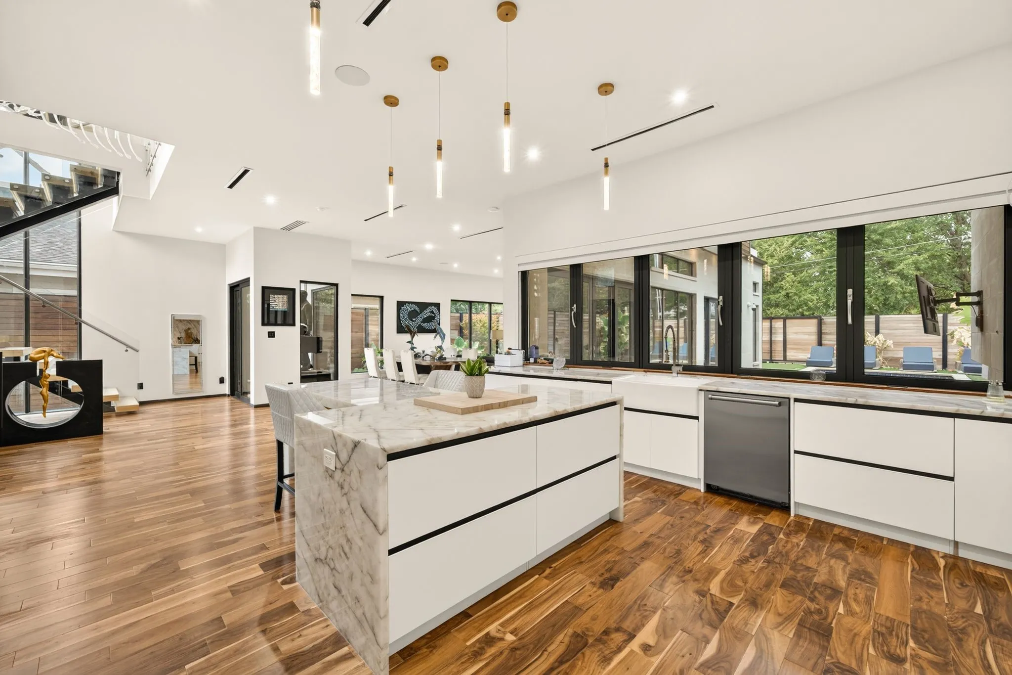 Modern kitchen with a waterfall island, white cabinetry, wood-finish flooring, and a large window overlooking the backyard