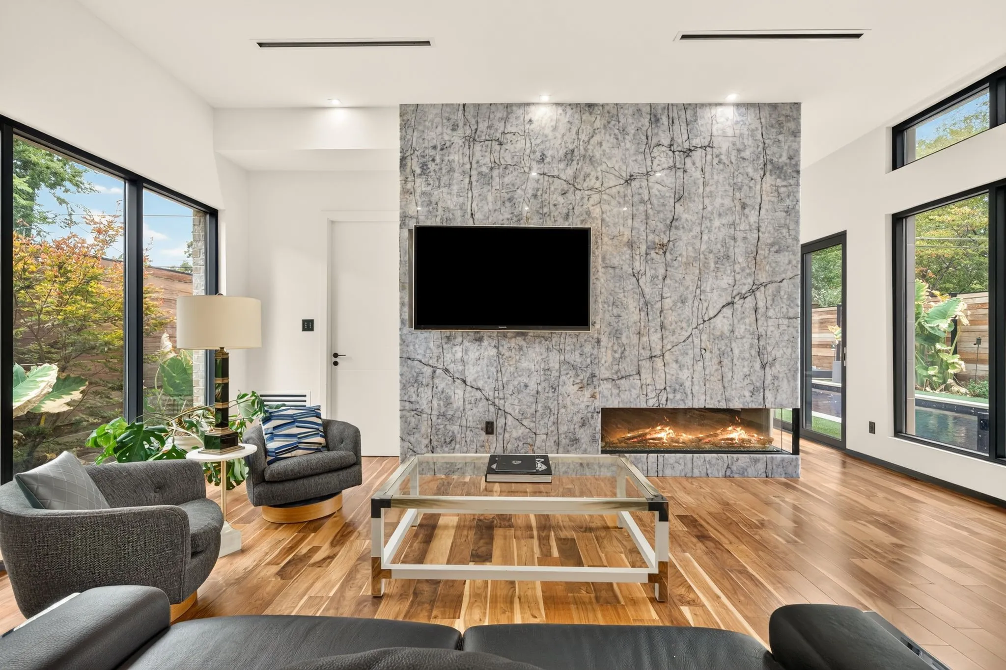 Spacious interior featuring a full-height stone-clad fireplace with an integrated linear firebox, wood flooring, and extensive black-framed windows