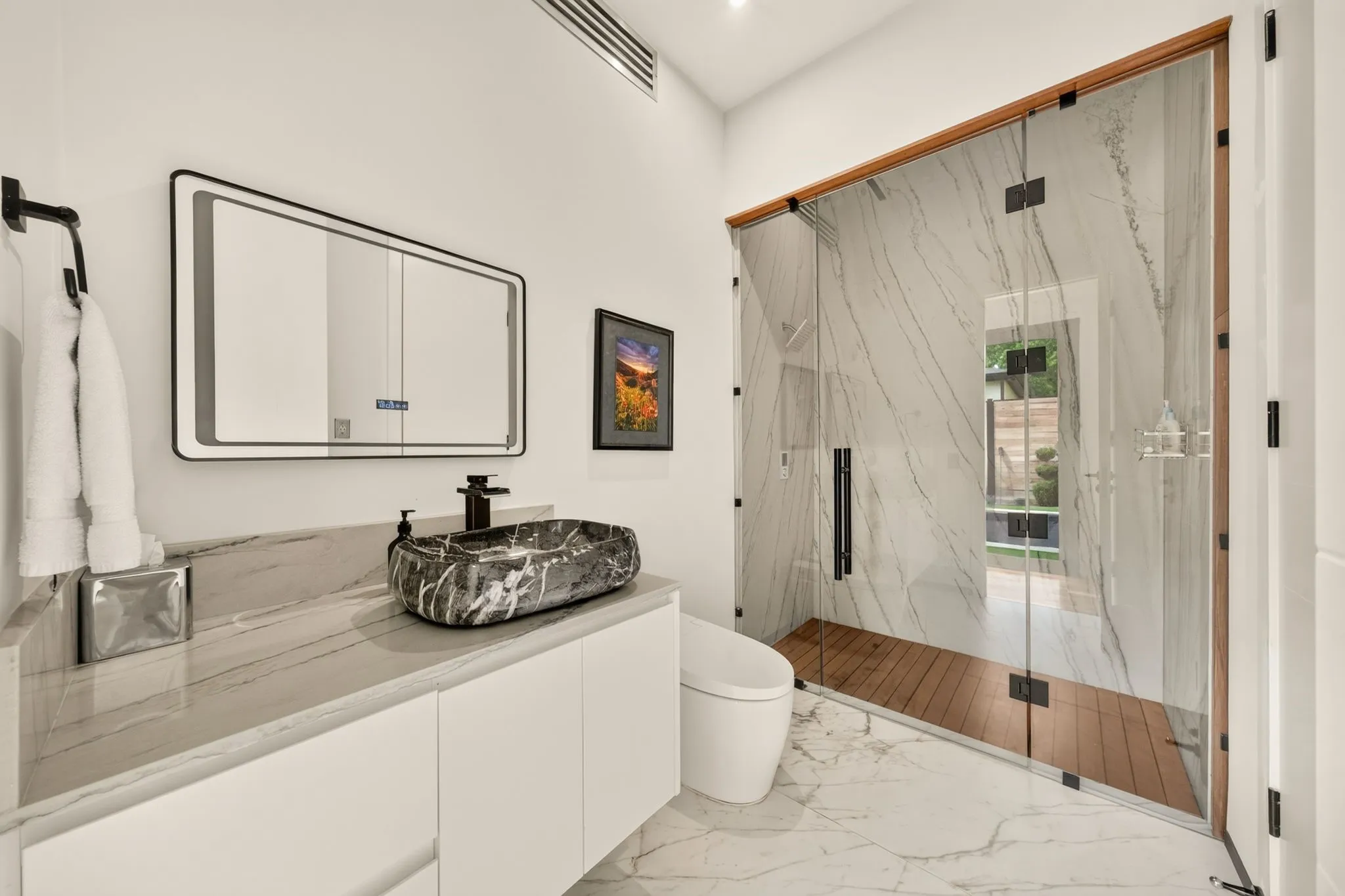 Floating vanity with a marbled vessel sink, illuminated mirror, walk-in shower with wood-finish flooring, and full-height tiled walls