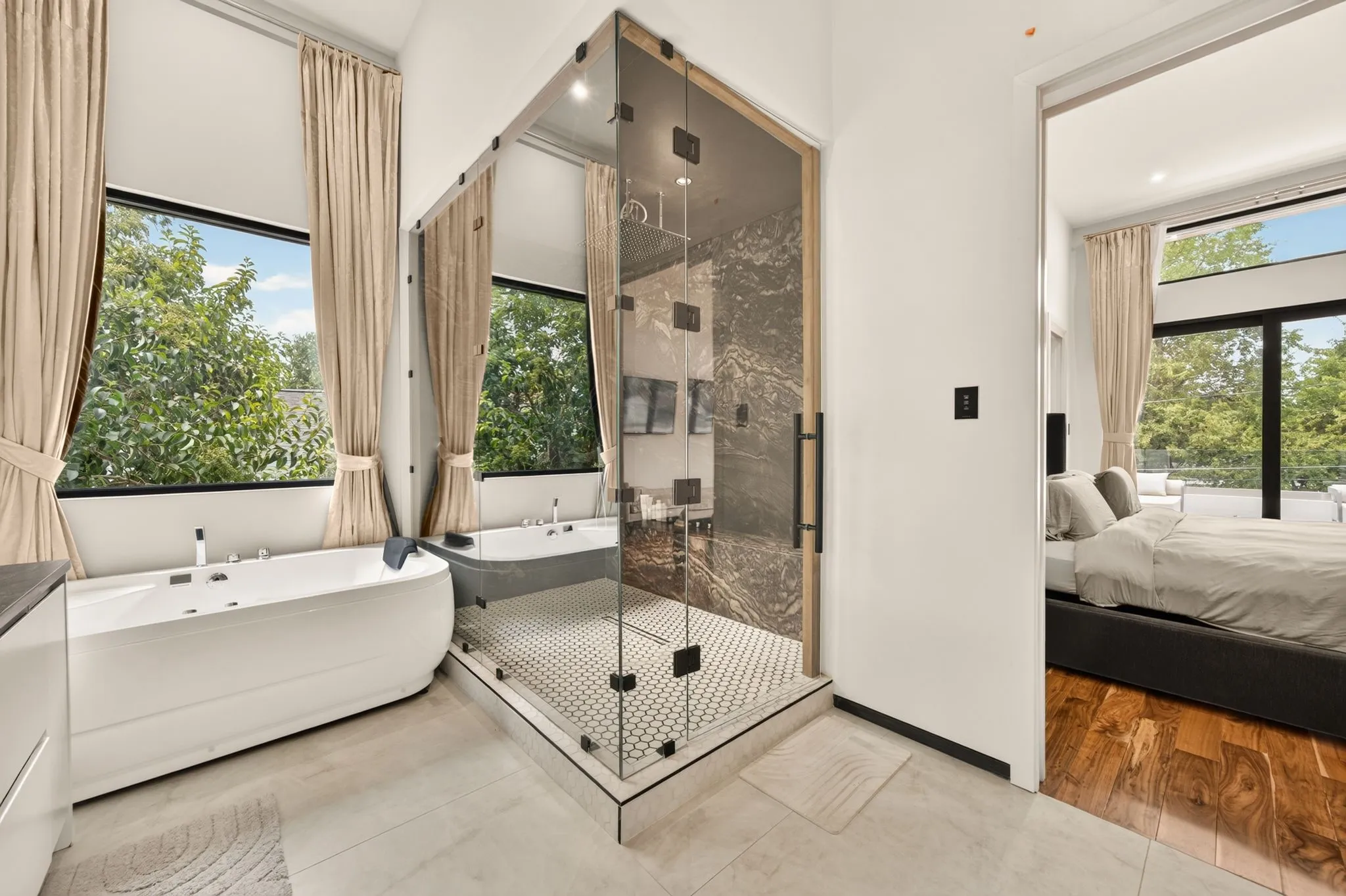 Freestanding soaking tub, glass-enclosed shower with dark stone-finish wall, hexagonal tile shower floor, and large windows with natural light