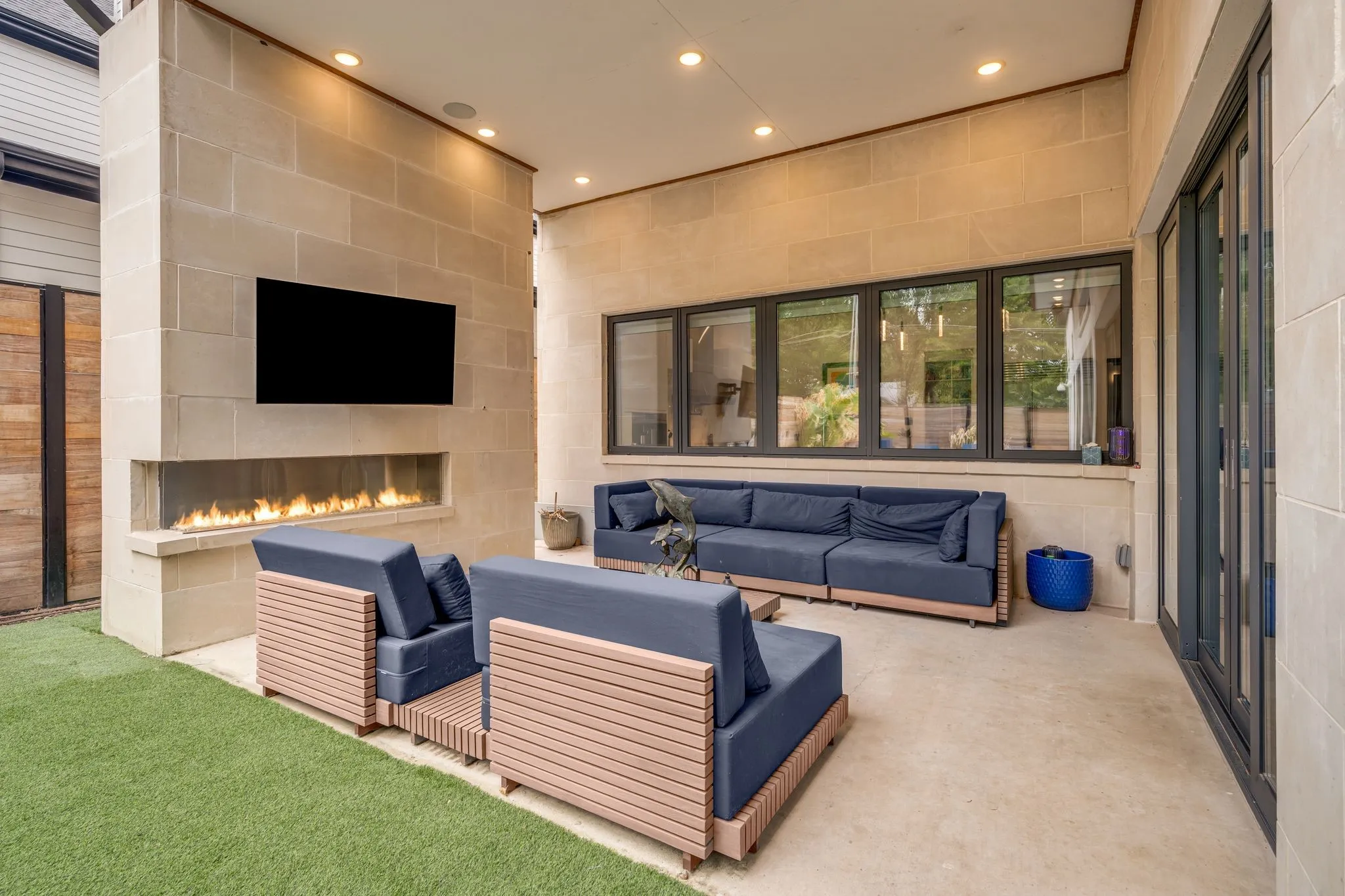 Outdoor living area featuring a stone accent wall, built-in linear fireplace, recessed lighting, and large multi-panel windows