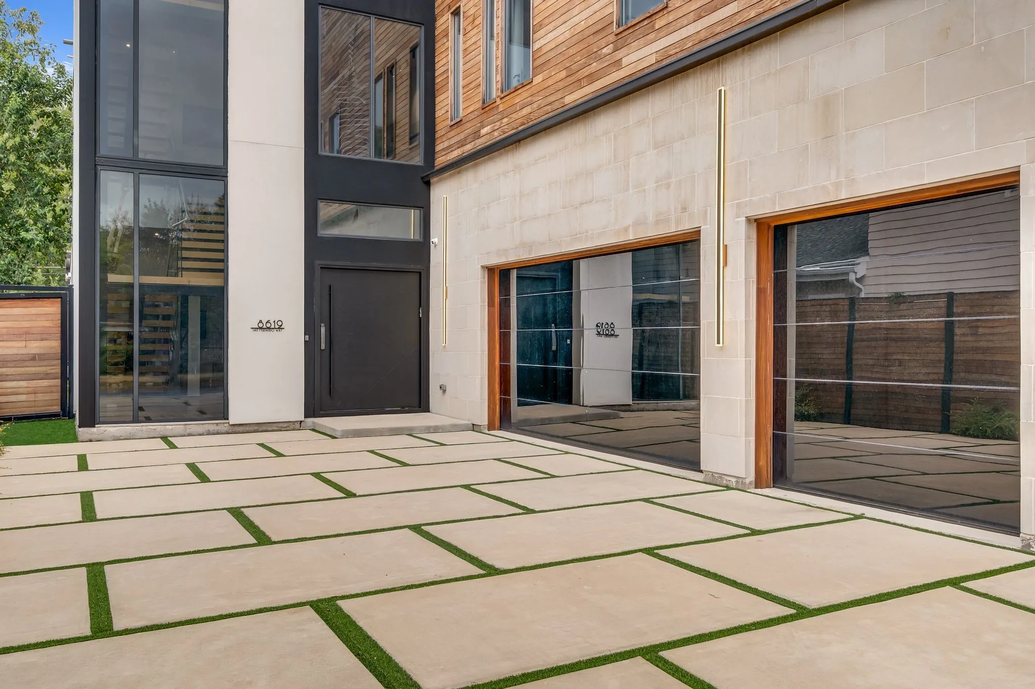 Modern exterior featuring a large glass facade, a prominent entry door, and a stone block garage area with two glass garage doors