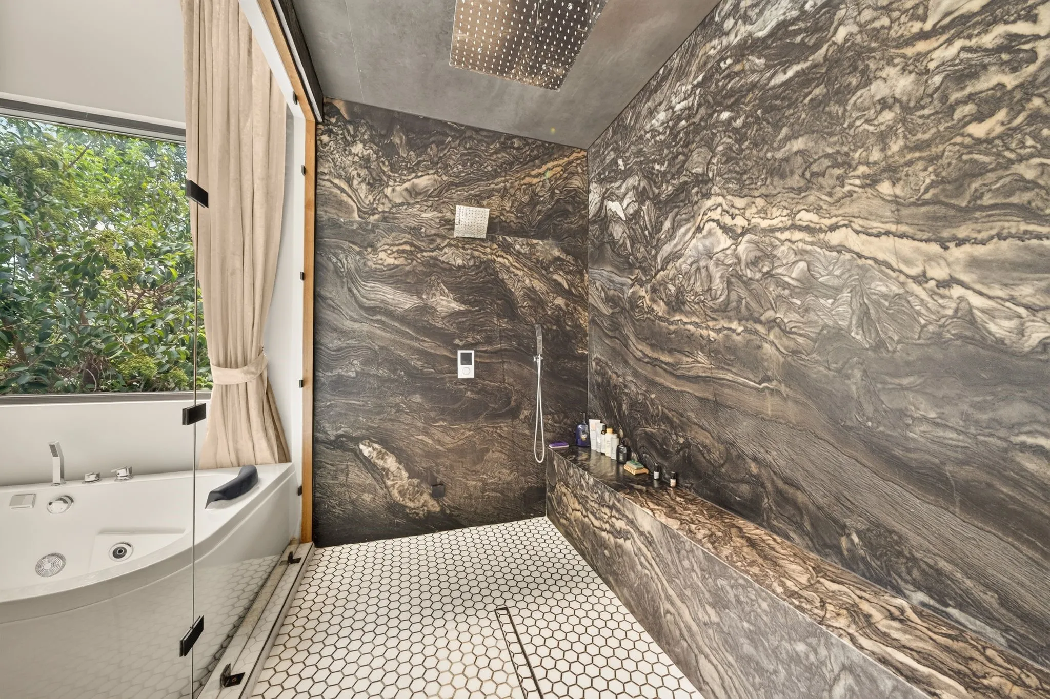 Full-height stone slab shower with integrated bench seating, hexagonal floor tiling, and a jetted soaking tub