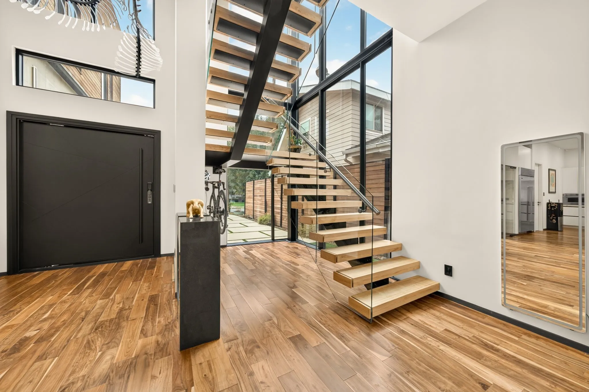 Wood-finish flooring, full-light entry, contemporary floating staircase with glass railing, and a black entry door