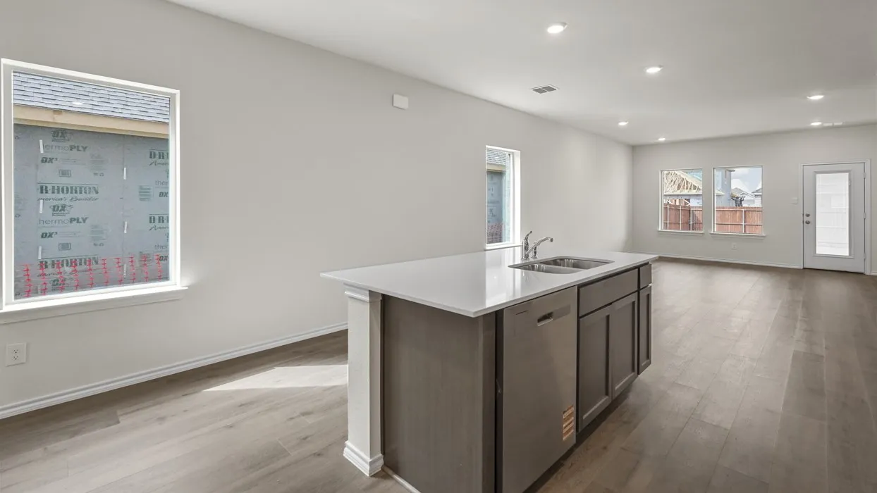 Open-concept living area with wood-finish flooring, recessed lighting, and a kitchen island featuring a double sink, stainless steel dishwasher, and cabinet storage