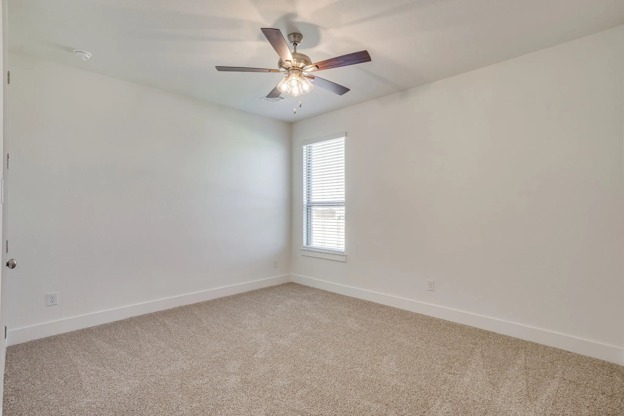 Neutral-toned carpeting, ceiling fan with integrated lighting, and a single window with blinds