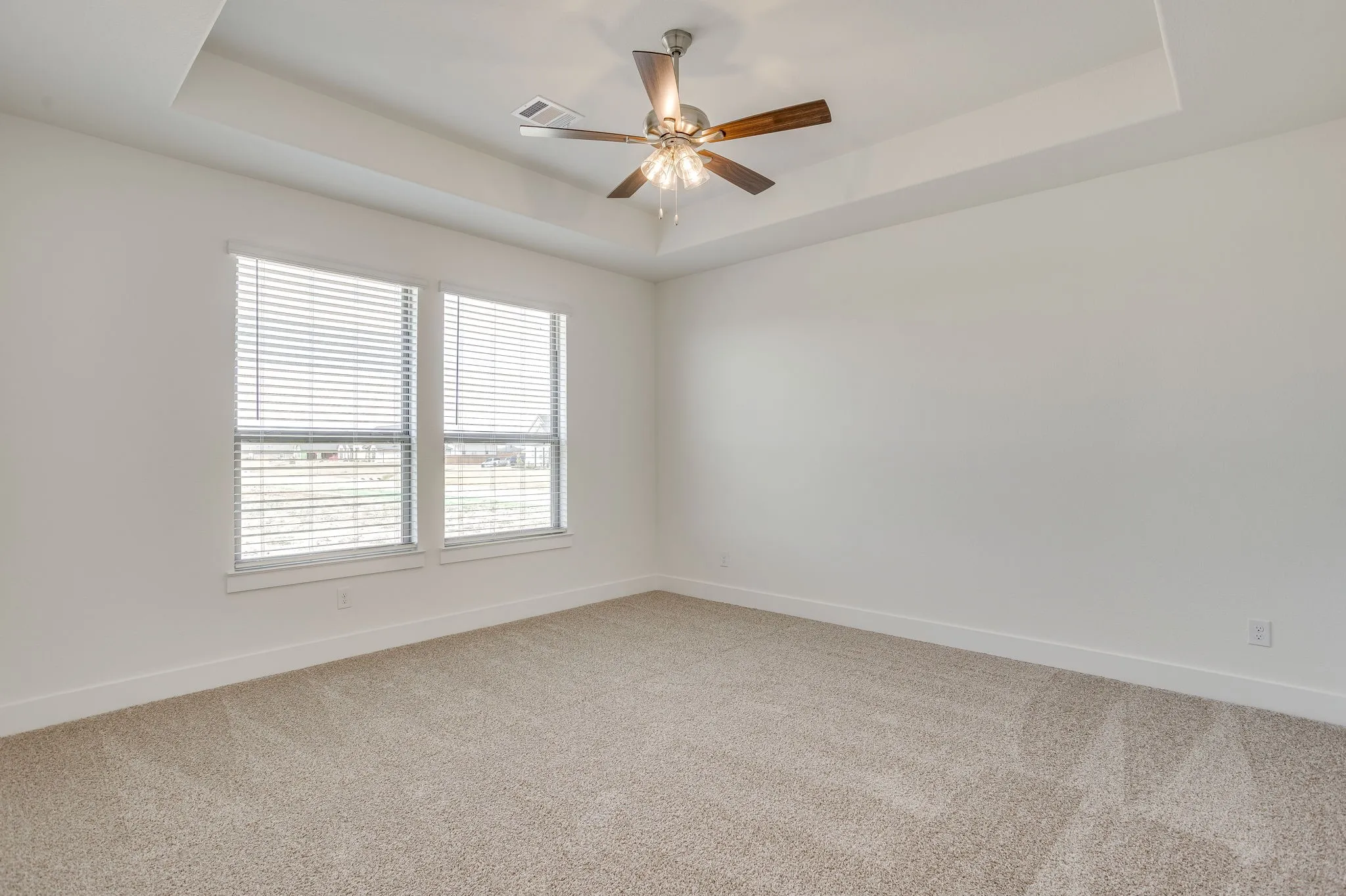 Tray ceiling with a ceiling fan, two windows with blinds, and neutral carpeting